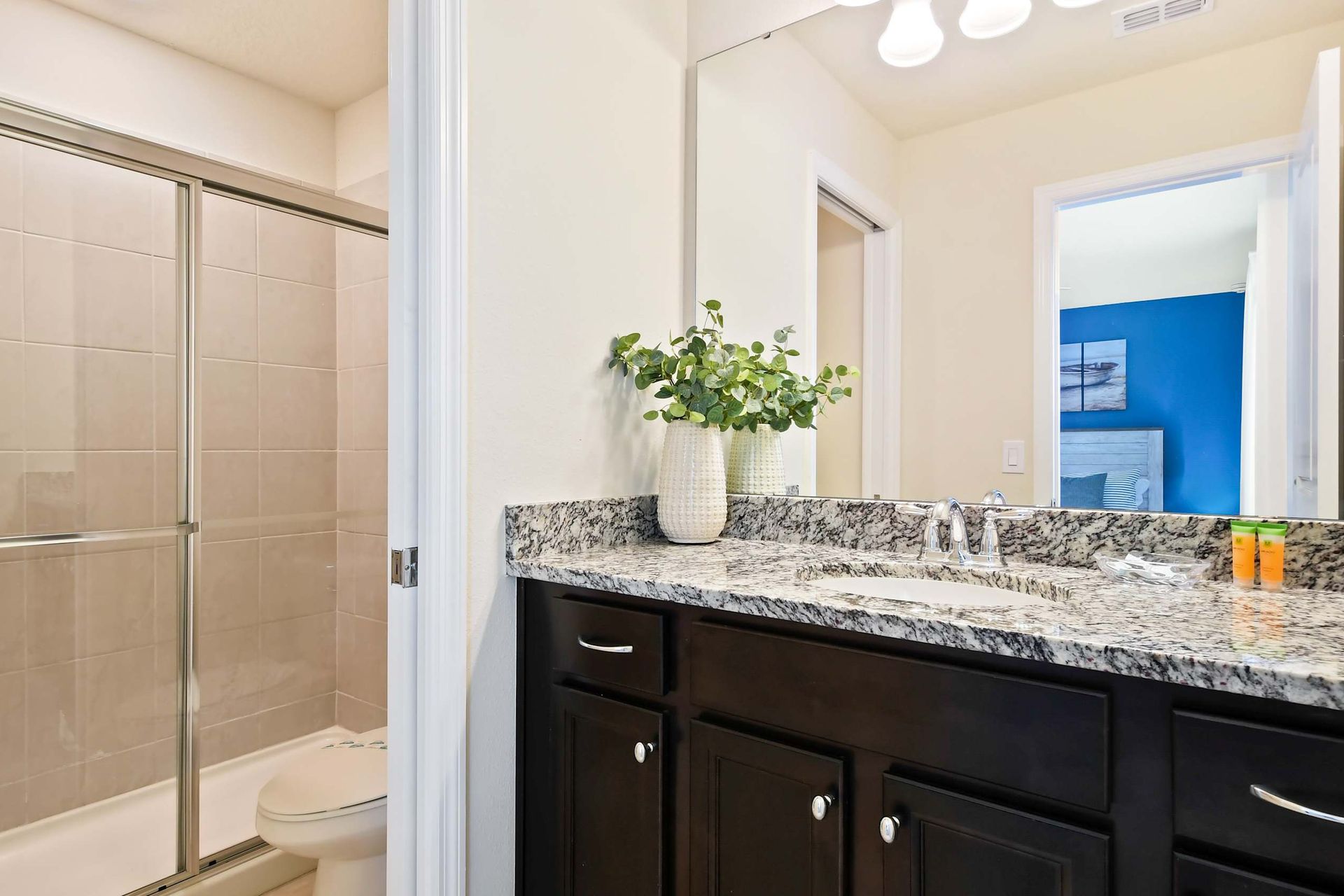 Modern bathroom with granite countertops, glass shower, and coastal-themed bedroom view.