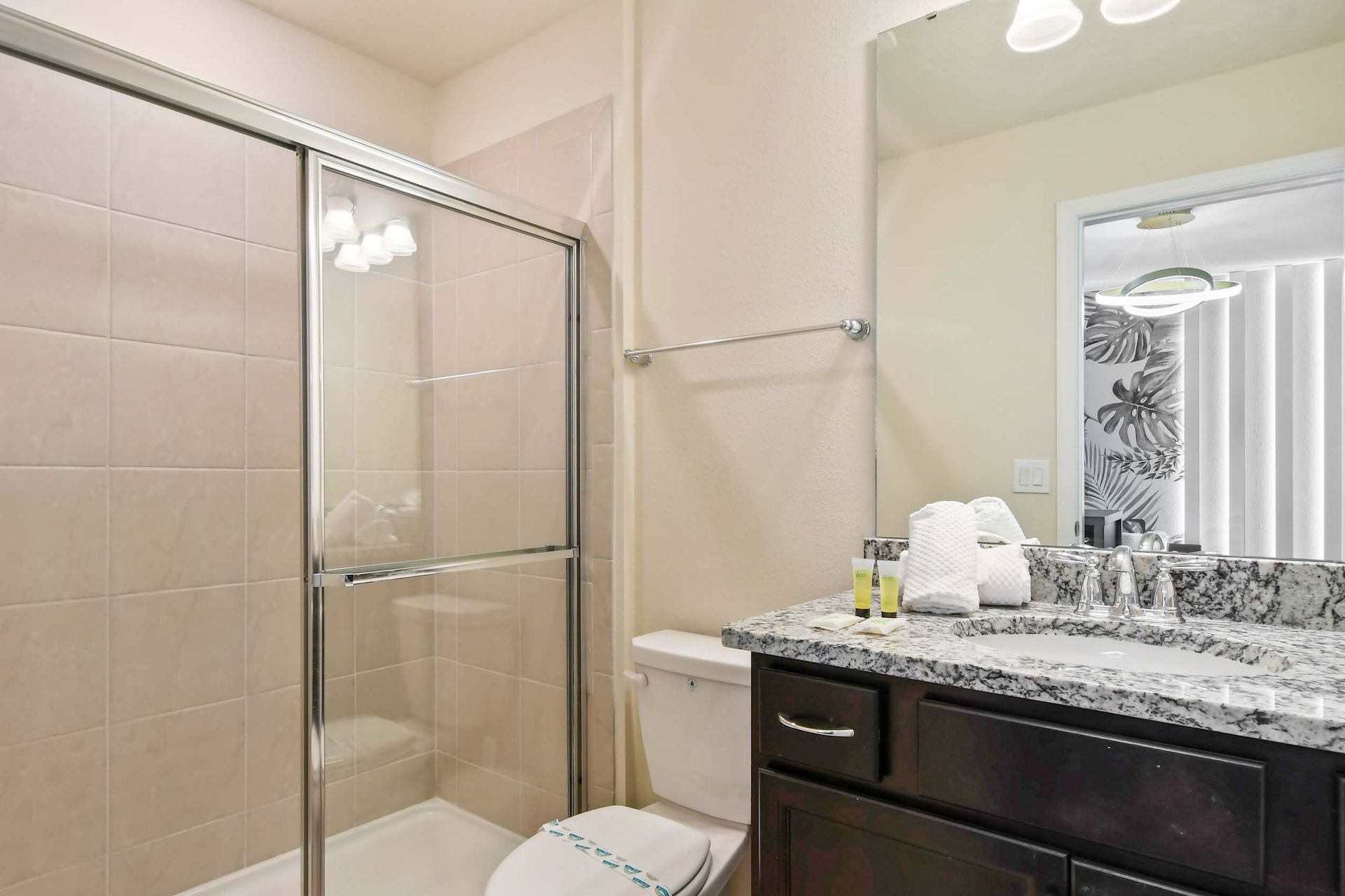 Modern bathroom with granite countertop, glass shower, and fresh amenities.