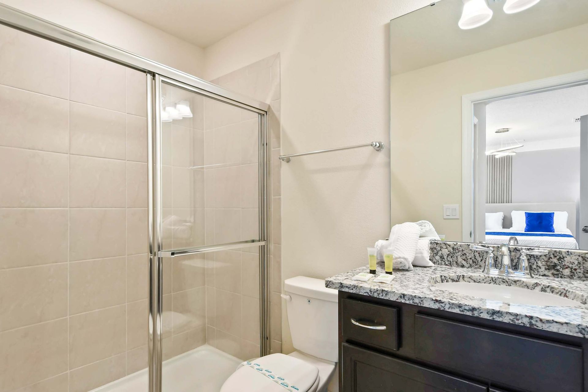 Modern bathroom with granite countertop, glass shower, and fresh amenities.