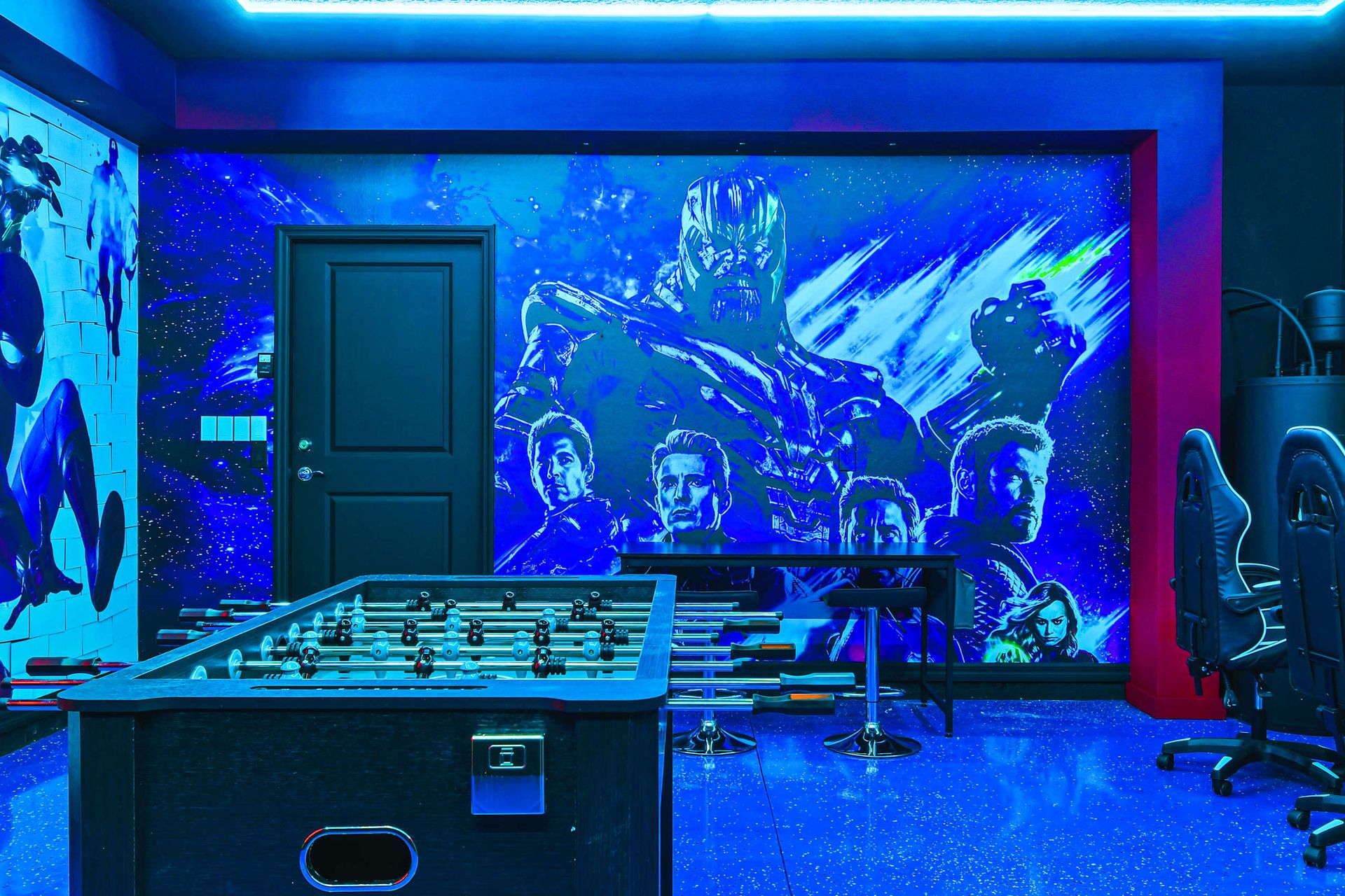 Marvel-themed game room with foosball, gaming chairs, and epic wall art.
