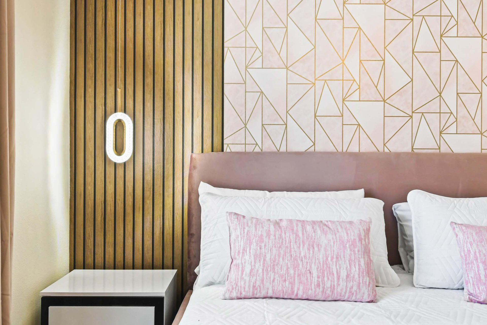 Stylish bedroom with geometric accents, soft pink tones, and modern lighting.