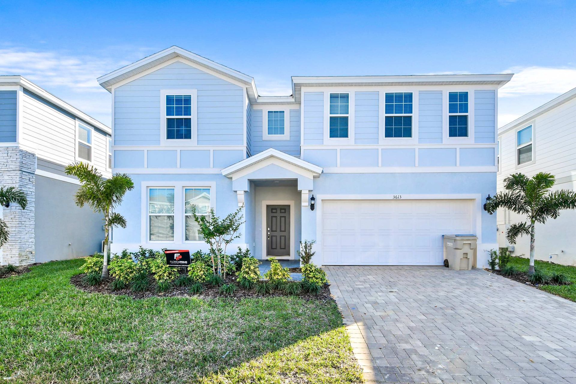 Modern two-story home with a spacious driveway, palm trees, and charming facade.