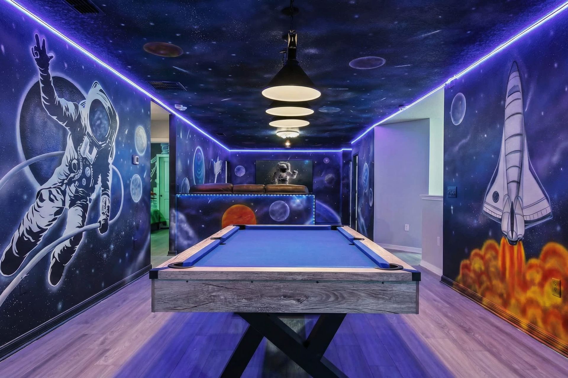 Cosmic game room with LED lights, rocket murals, and a sleek blue pool table.