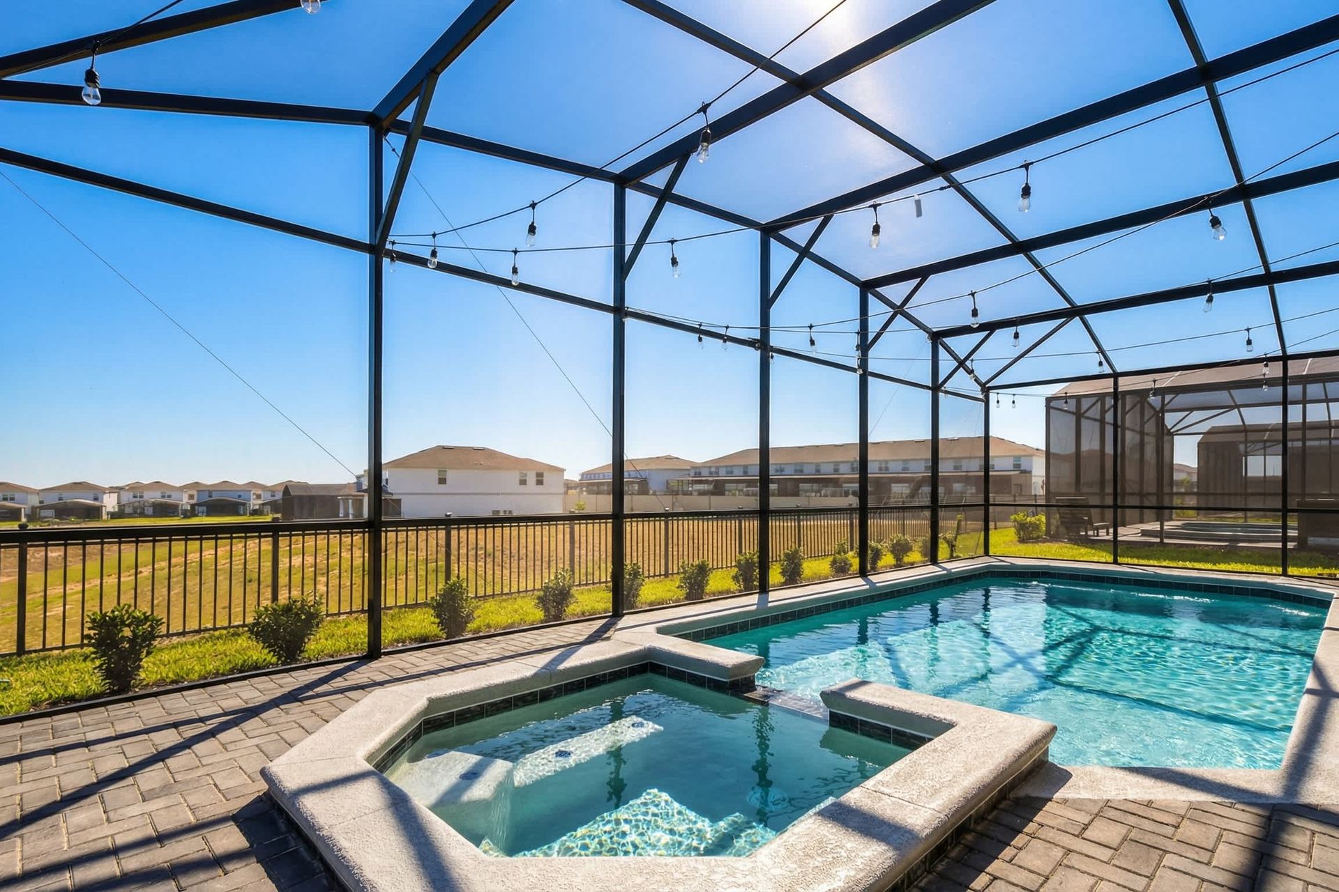 Sunny screened-in pool and spa with string lights, open views, and resort-style charm.