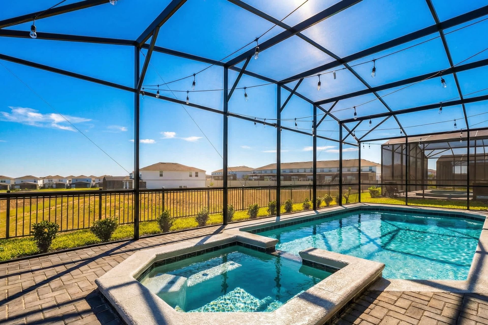 Sunny screened-in pool and spa with string lights, open views, and resort-style charm.