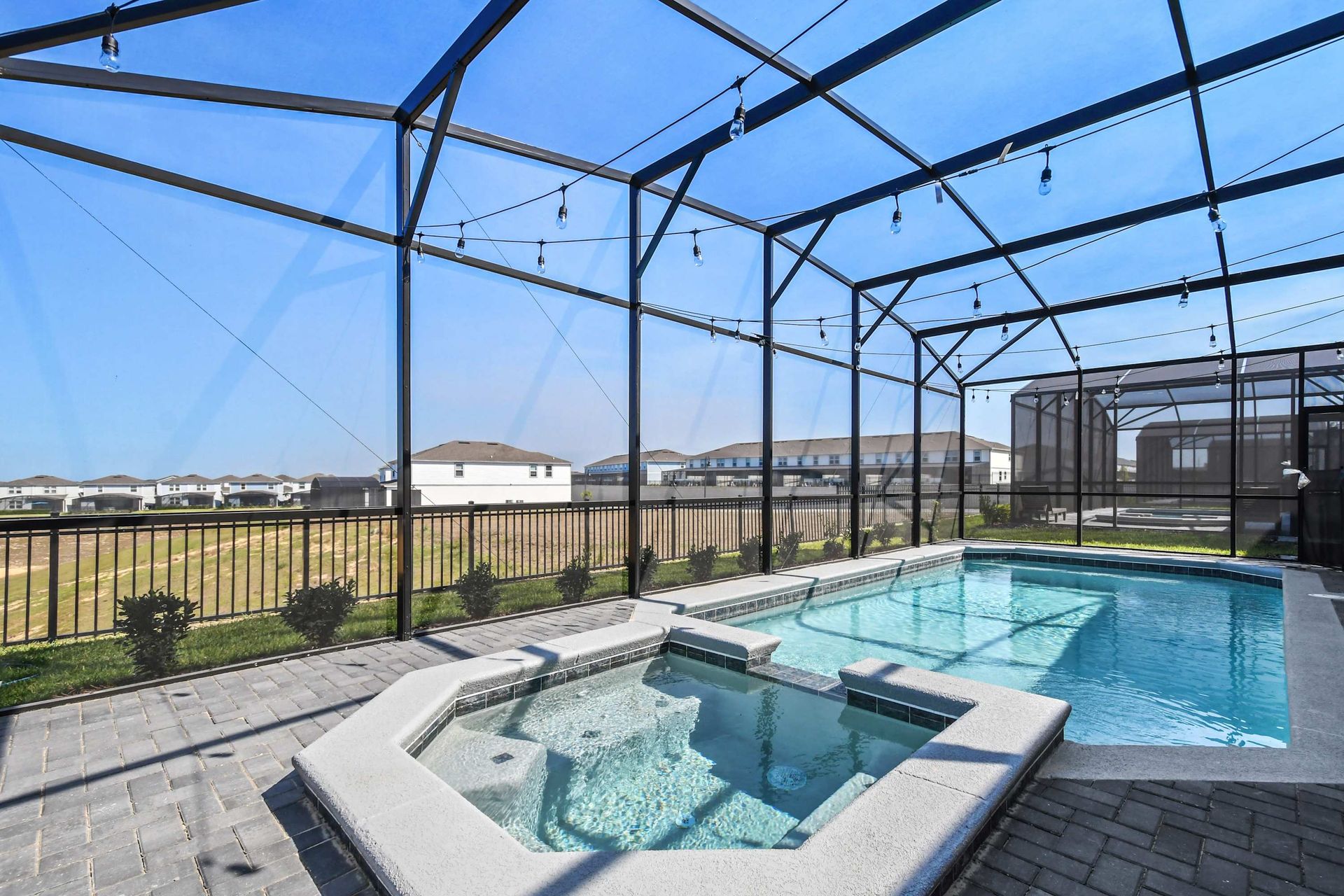 Sunny screened-in pool and spa with string lights, open views, and resort-style charm.