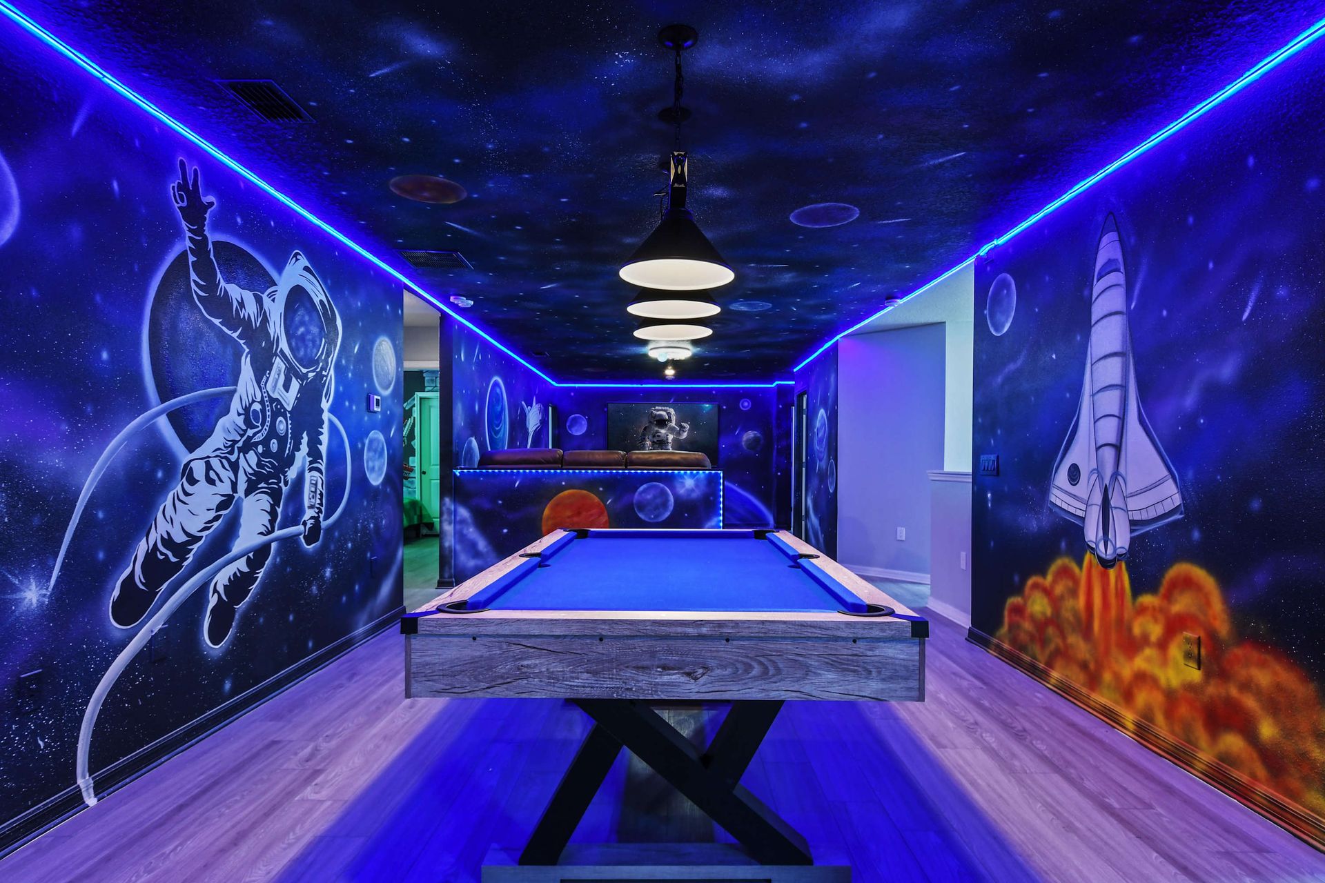 Cosmic game room with LED lights, rocket murals, and a sleek blue pool table.