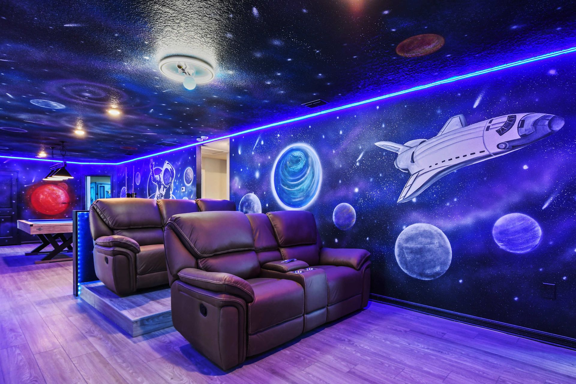 Out-of-this-world theater room with galaxy murals, glowing lights, and plush seating.