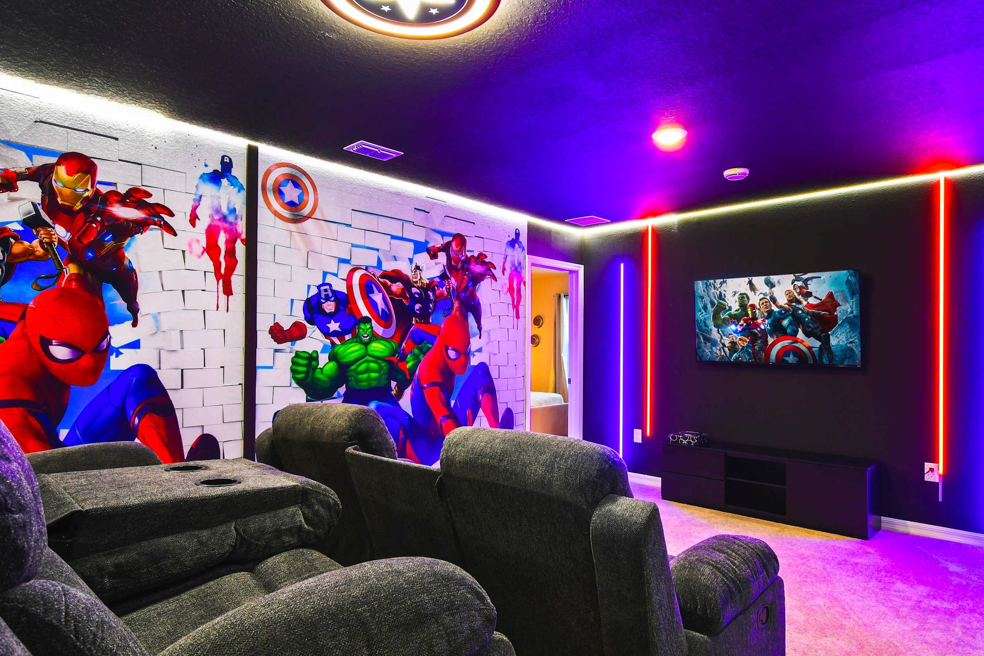 Marvel-themed home theater with neon lights, recliners, and epic superhero murals.