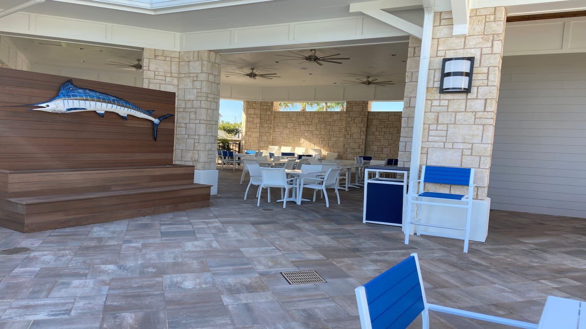 Spacious covered patio with coastal decor, dining tables, ceiling fans, and stage

