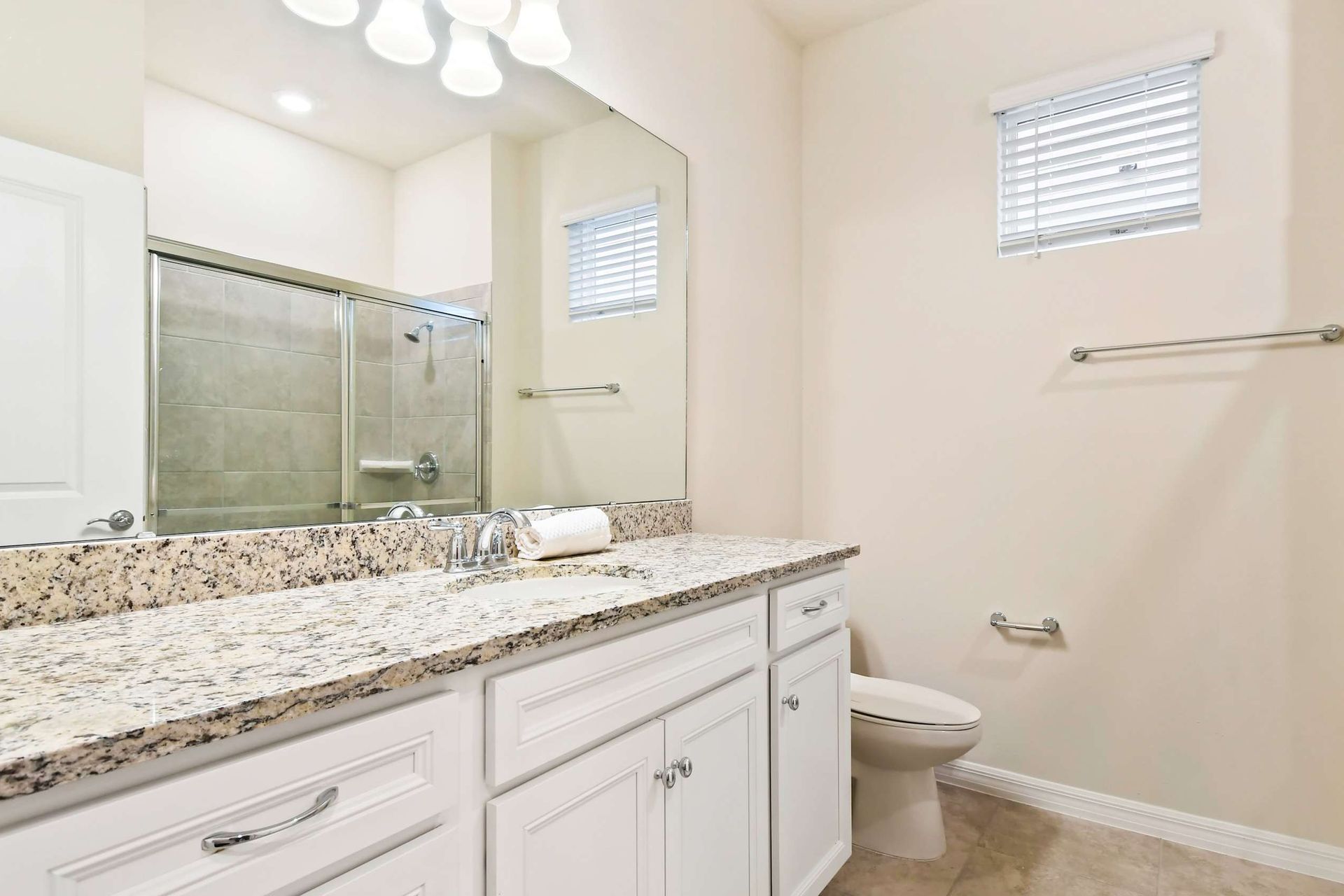 Bright modern bathroom with granite vanity, large mirror, and plenty of natural light
