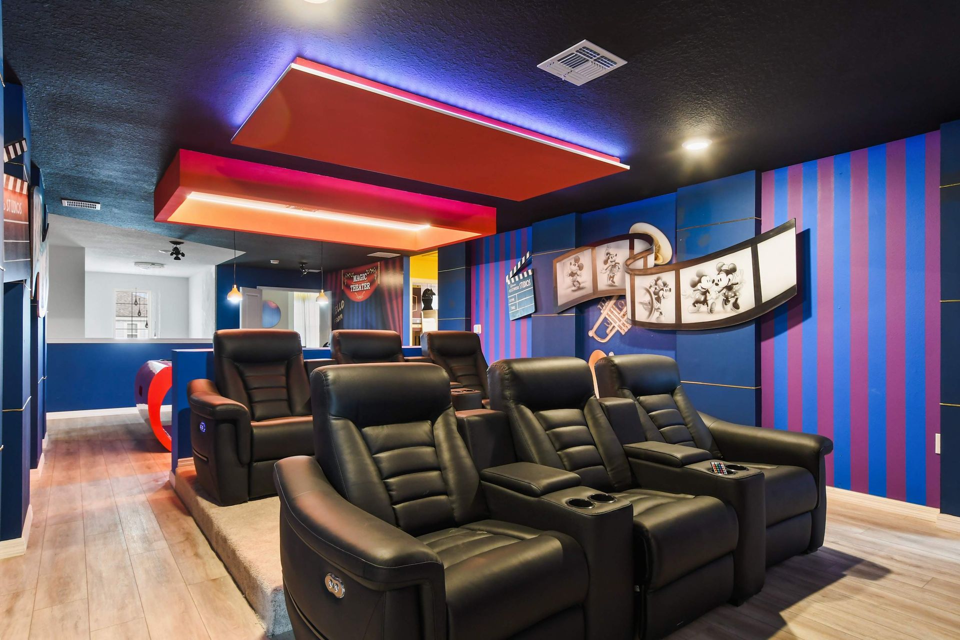 Disney-style home theater with tiered leather recliners, playful wall art, and cozy ambiance.