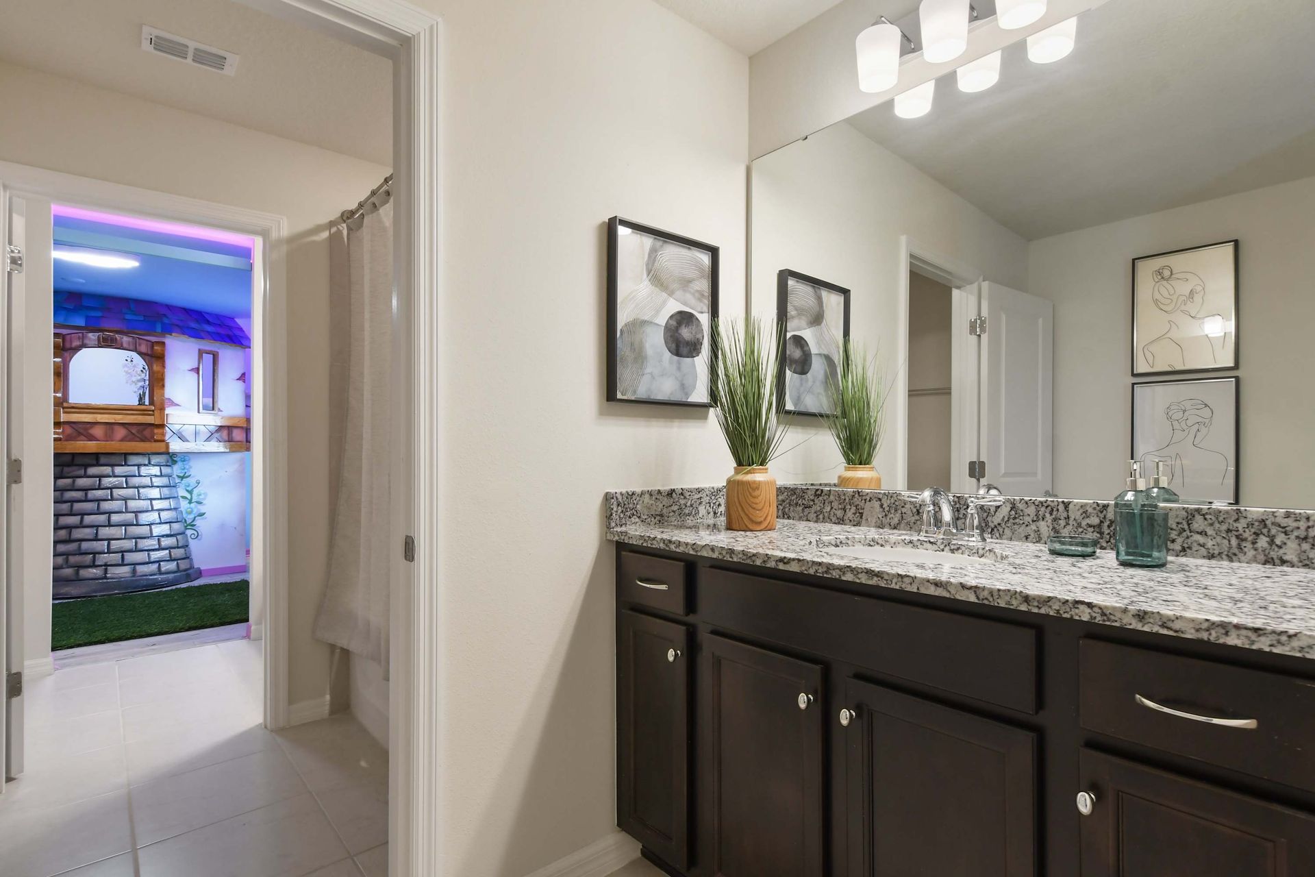Chic bathroom with granite double vanity, modern art, and access to themed room.
