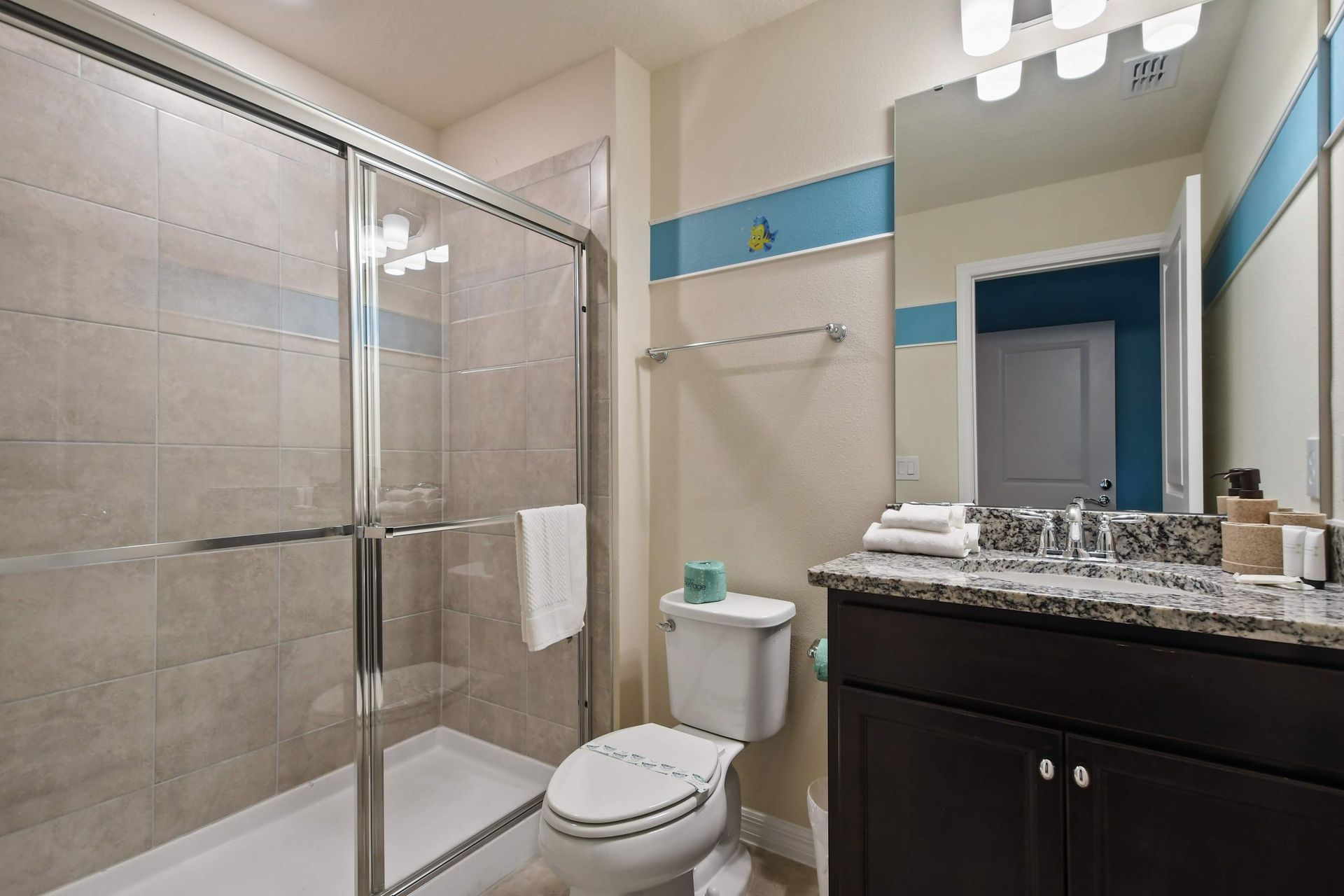 Modern bathroom with walk-in shower, granite vanity, and playful accent decor.