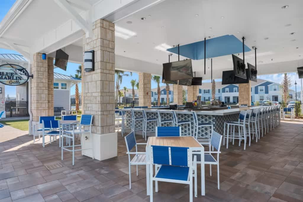 Open-air resort bar with multiple TVs, modern seating, and views of palm trees

