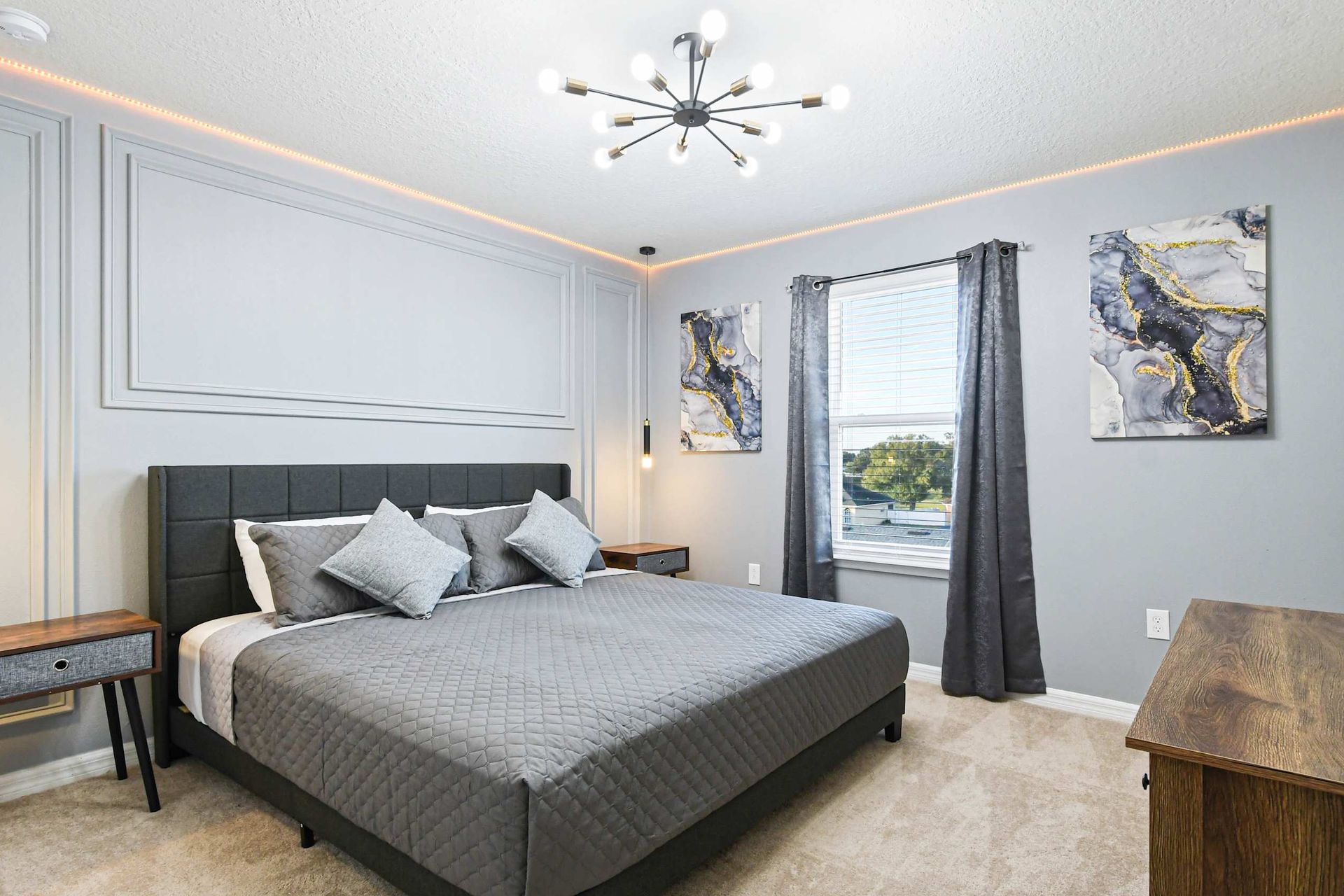 Modern bedroom with king bed, sleek lighting, abstract art, and cozy gray tones.