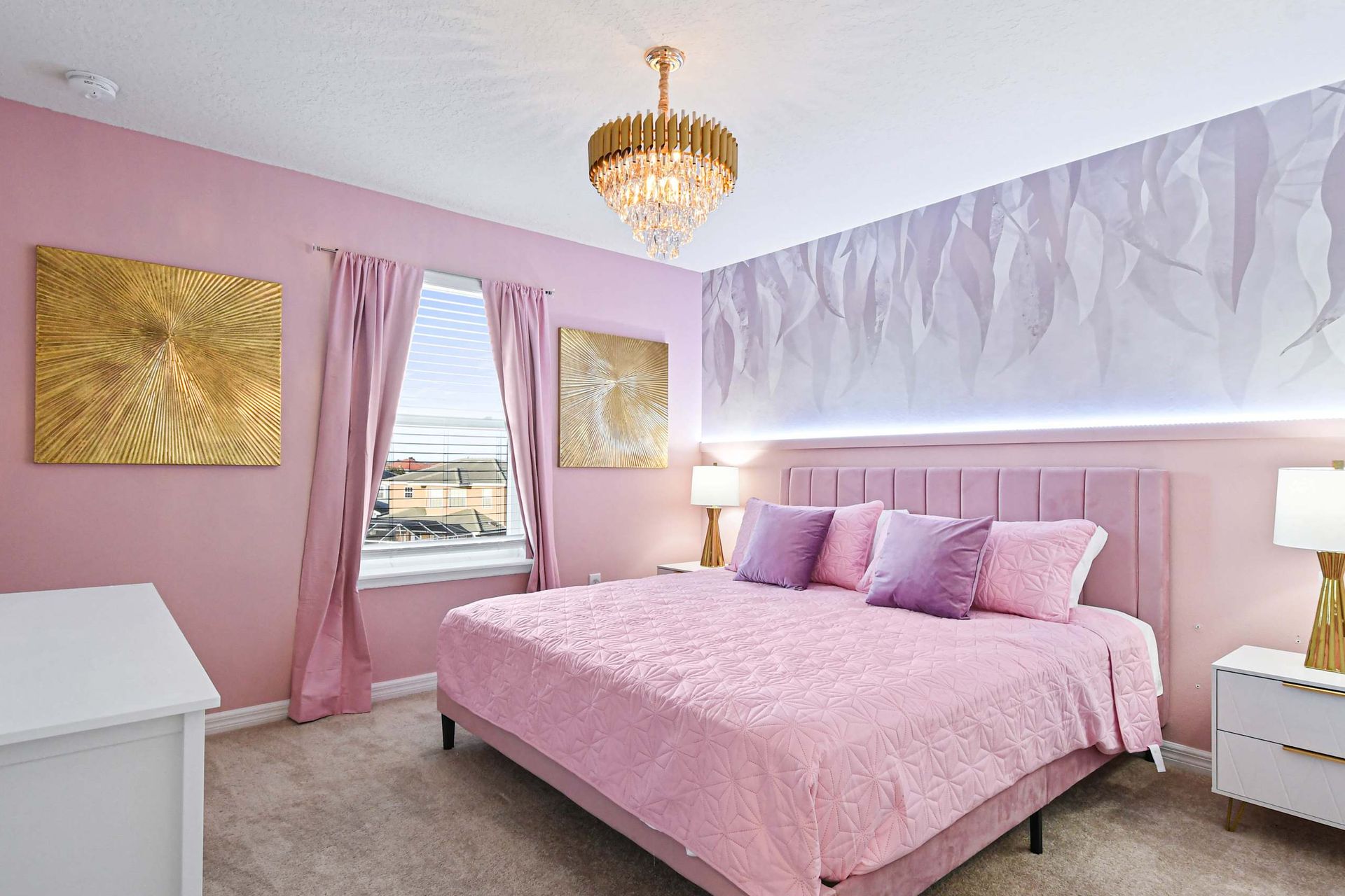 Glam pink bedroom with king bed, gold accents, chandelier, and elegant flair.