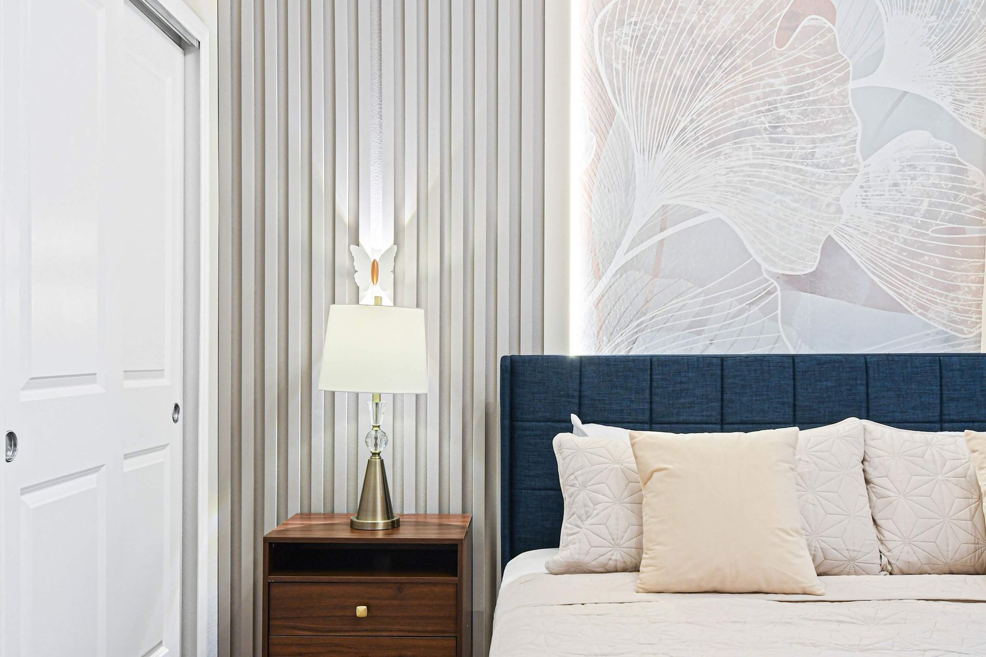 Elegant bedroom corner with modern lamp, soft lighting, and floral accent wall.