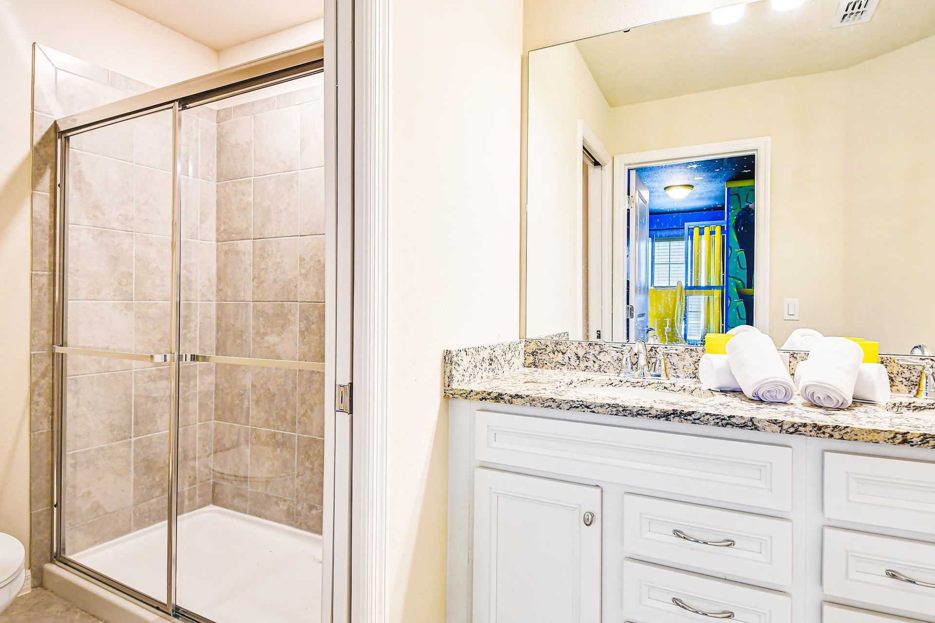 Granite vanity bathroom with glass shower and peek into fun Minions-themed room.