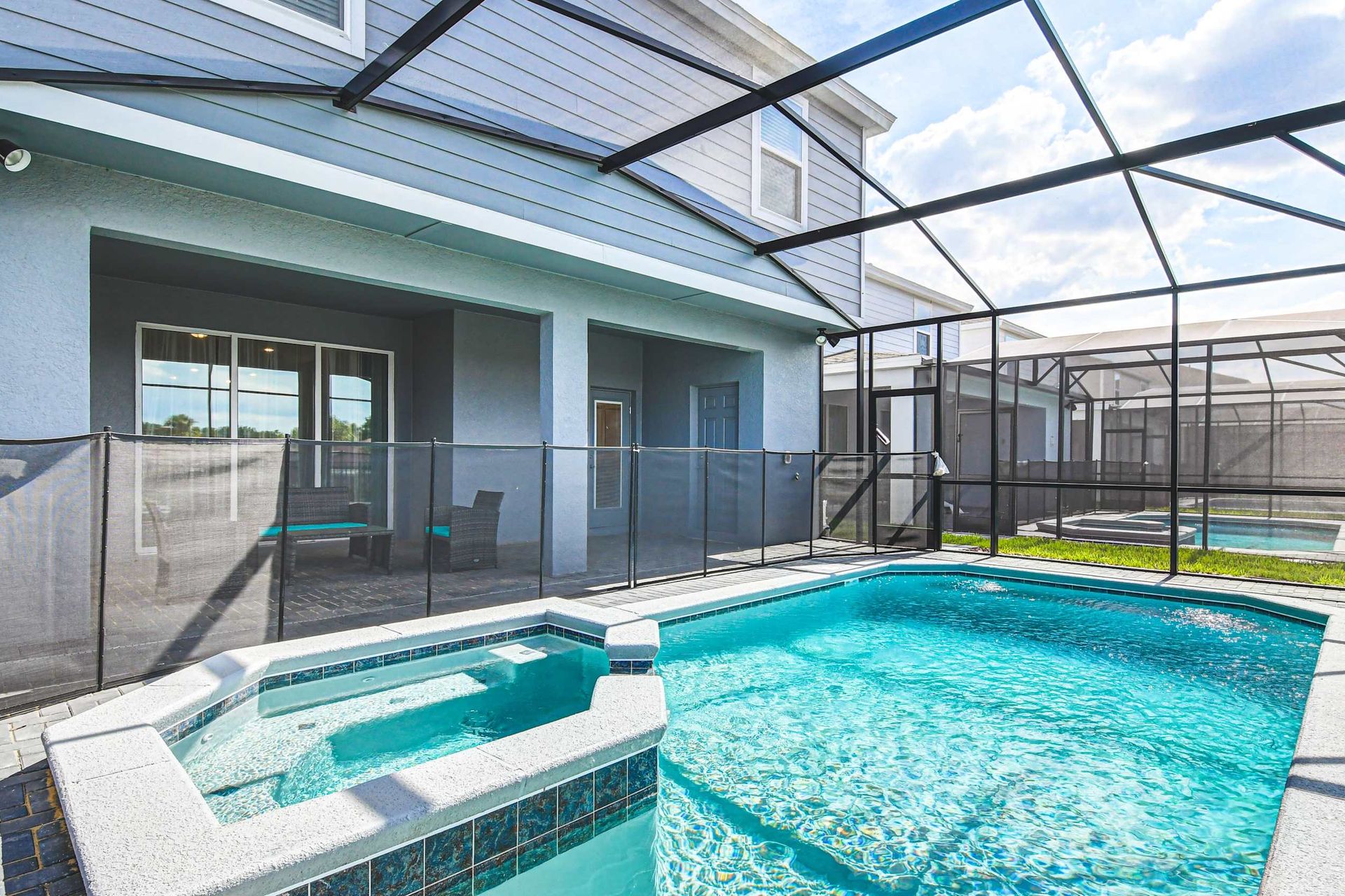 Screened-in private pool and spa with patio seating and full safety fencing.