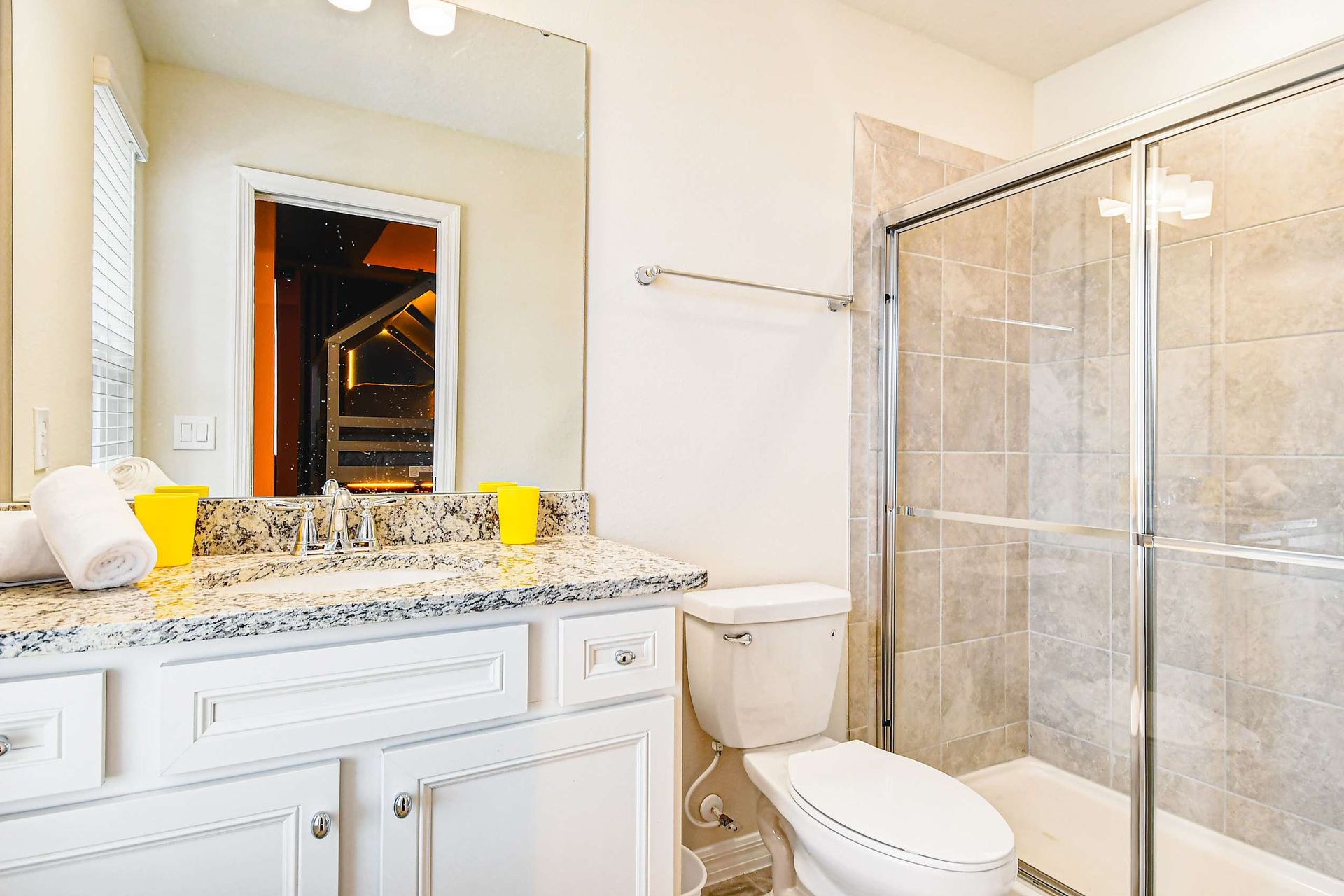 Bright bathroom with granite vanity, glass shower, and view into themed bedroom.