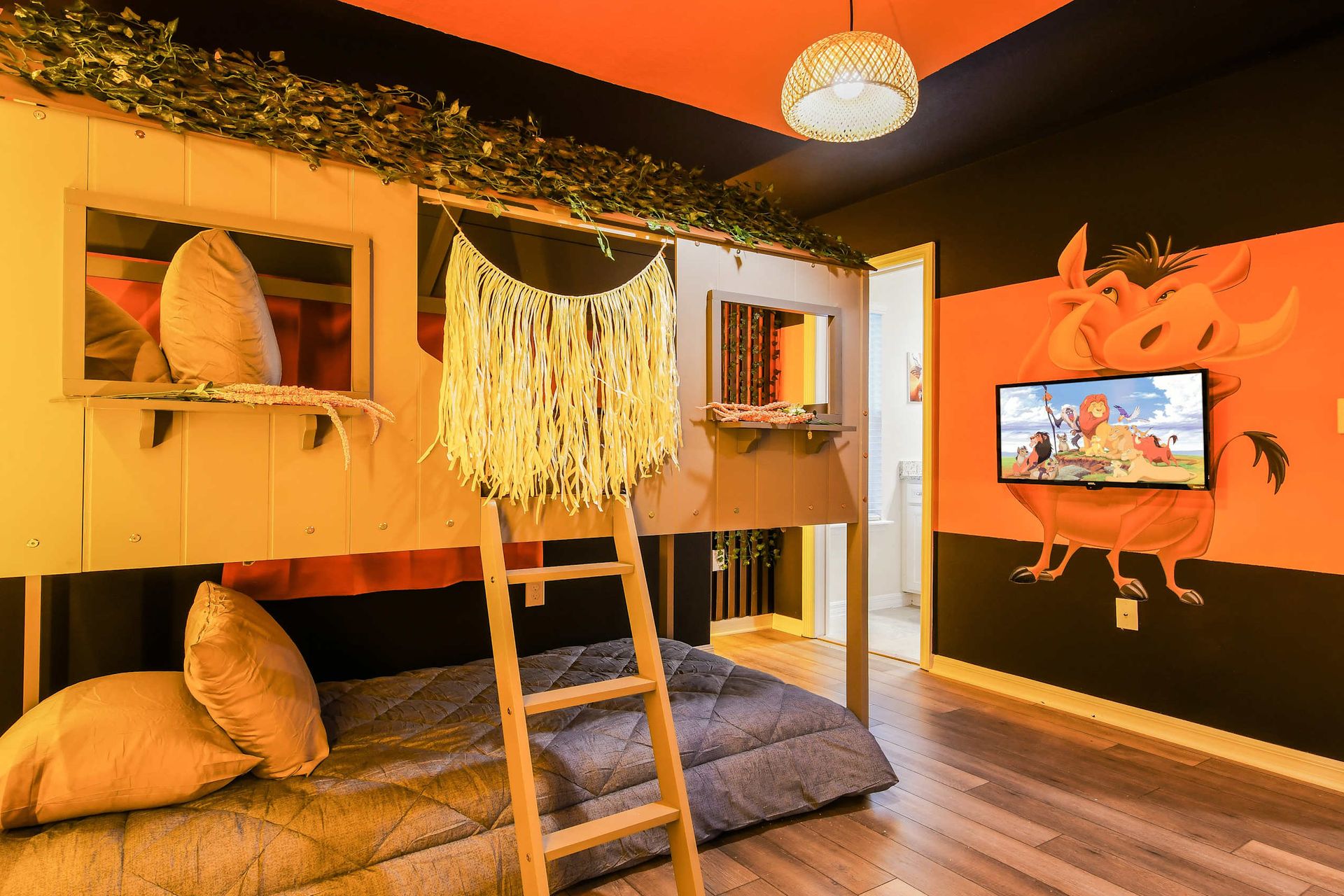 Jungle-themed kids’ room with treehouse bunk, TV, and Lion King mural.