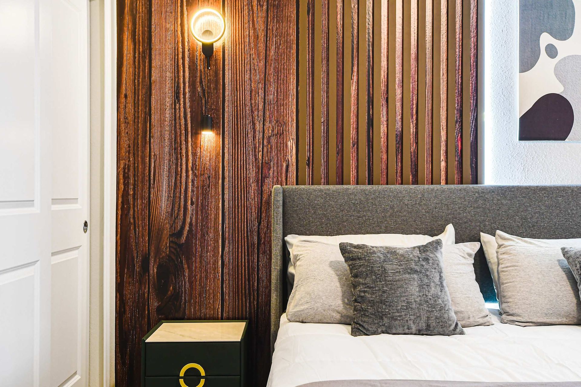 Modern bedroom detail with wood panel accent wall, soft lighting, and plush bedding.