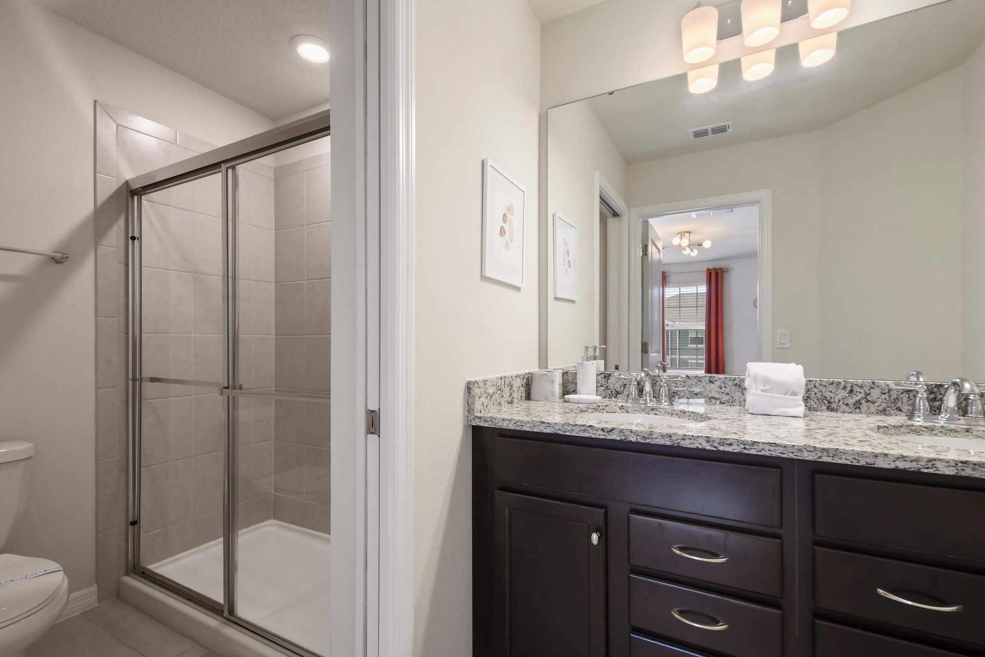 Modern bathroom with granite double vanity, glass walk-in shower, and bright lighting.