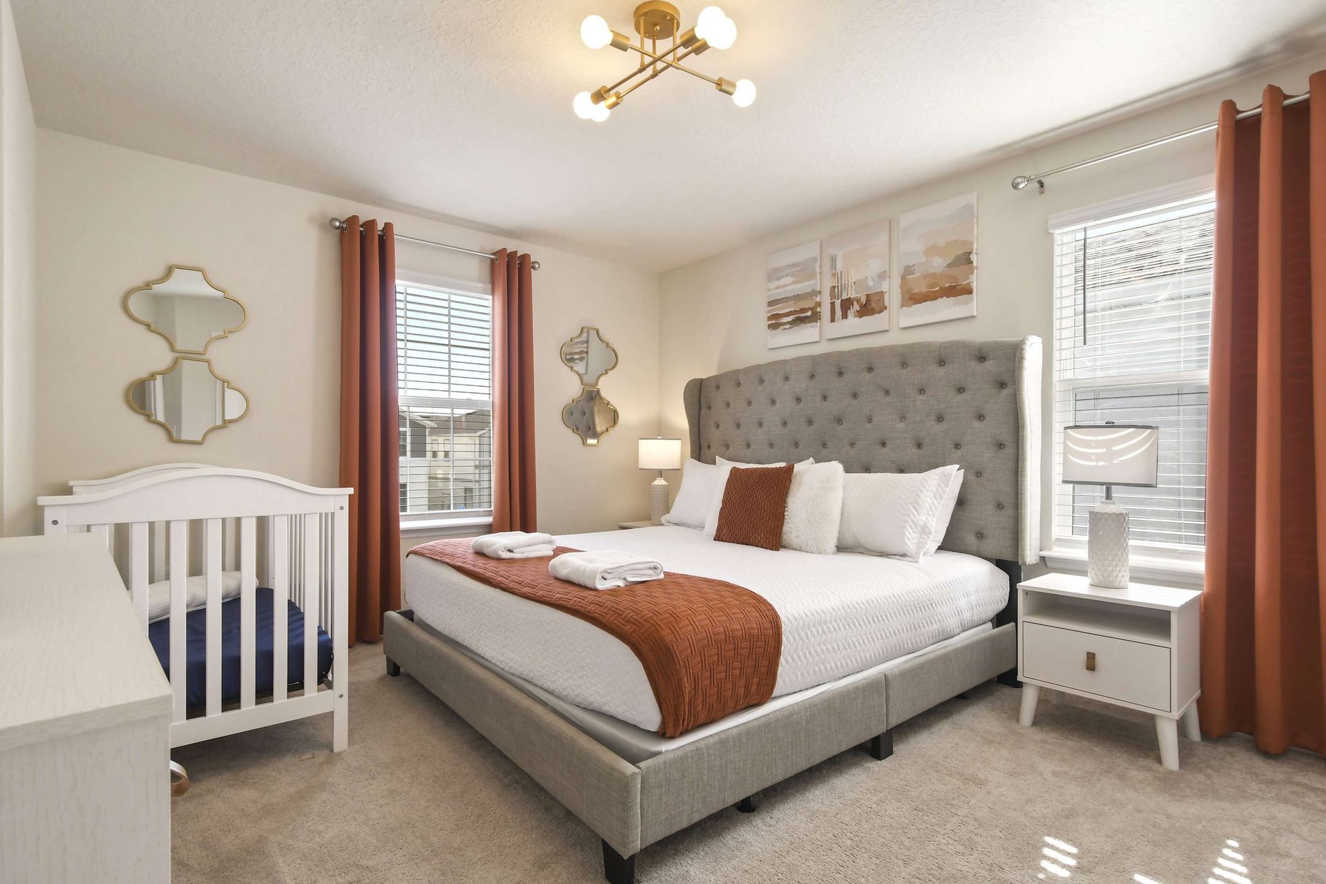 Cozy primary suite with king bed, crib, modern decor, and warm natural light.