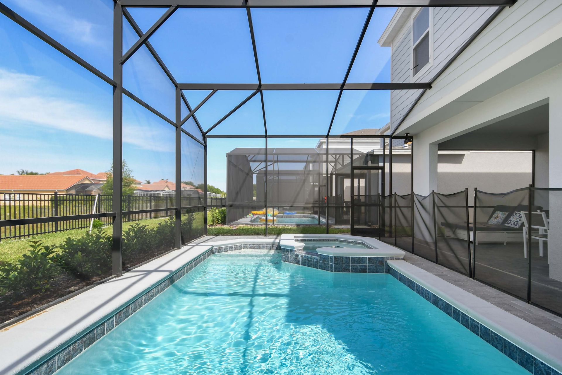 Screened private pool and spa with sunny patio, safety gate, and outdoor seating.