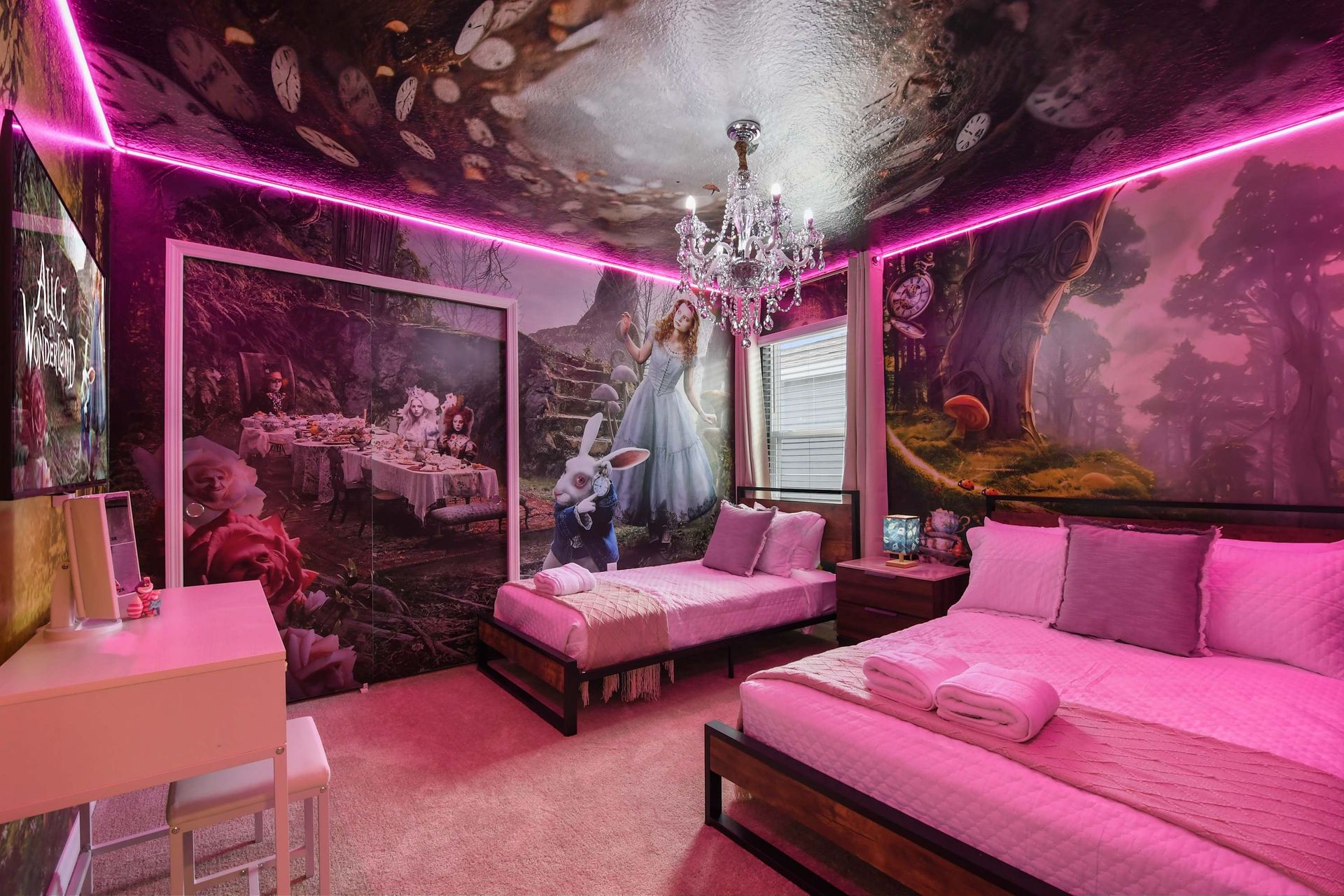 Whimsical Alice in Wonderland bedroom with dreamy murals, chandelier, and pink glow.