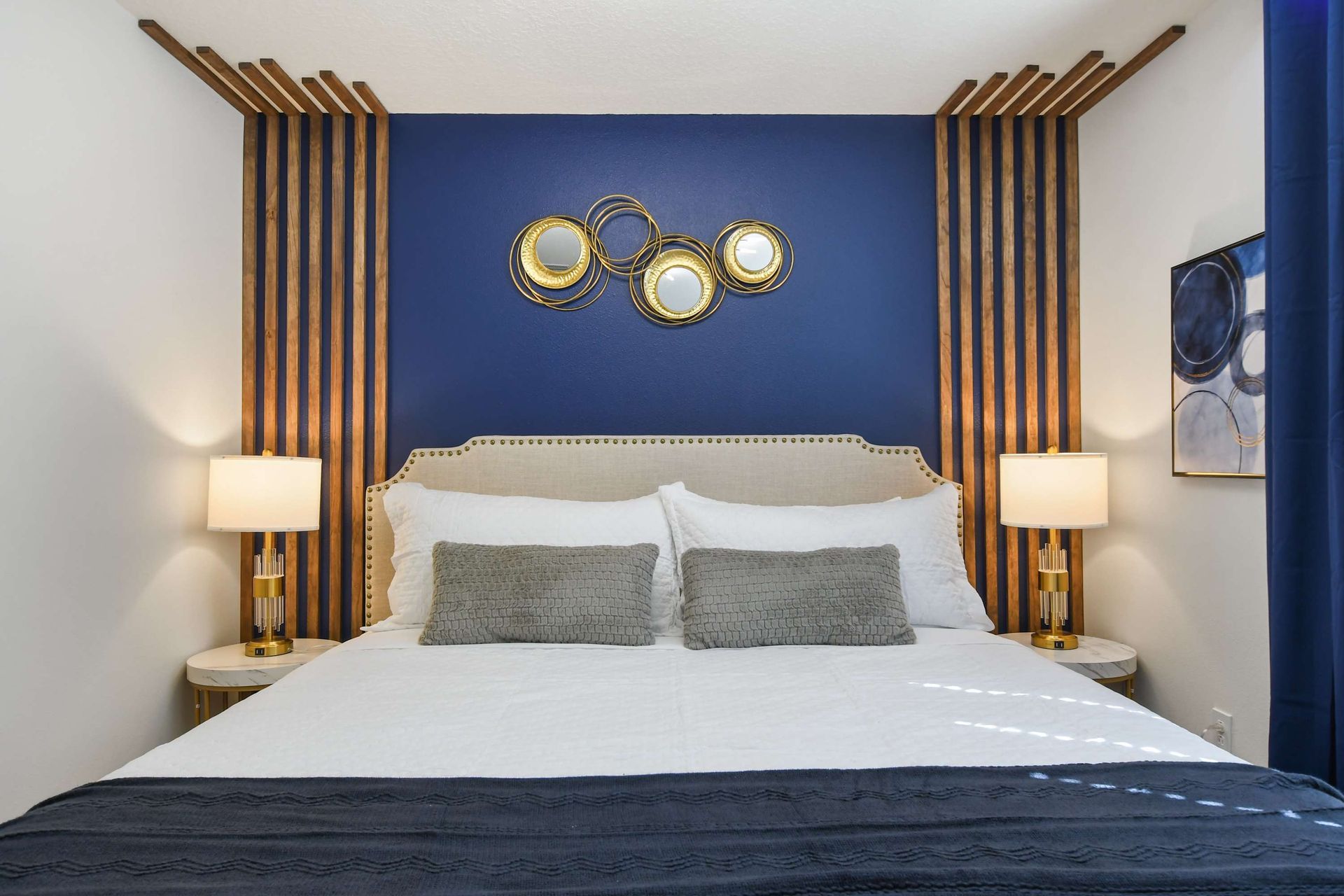 Elegant king bedroom with navy feature wall, gold accents, and modern lighting.