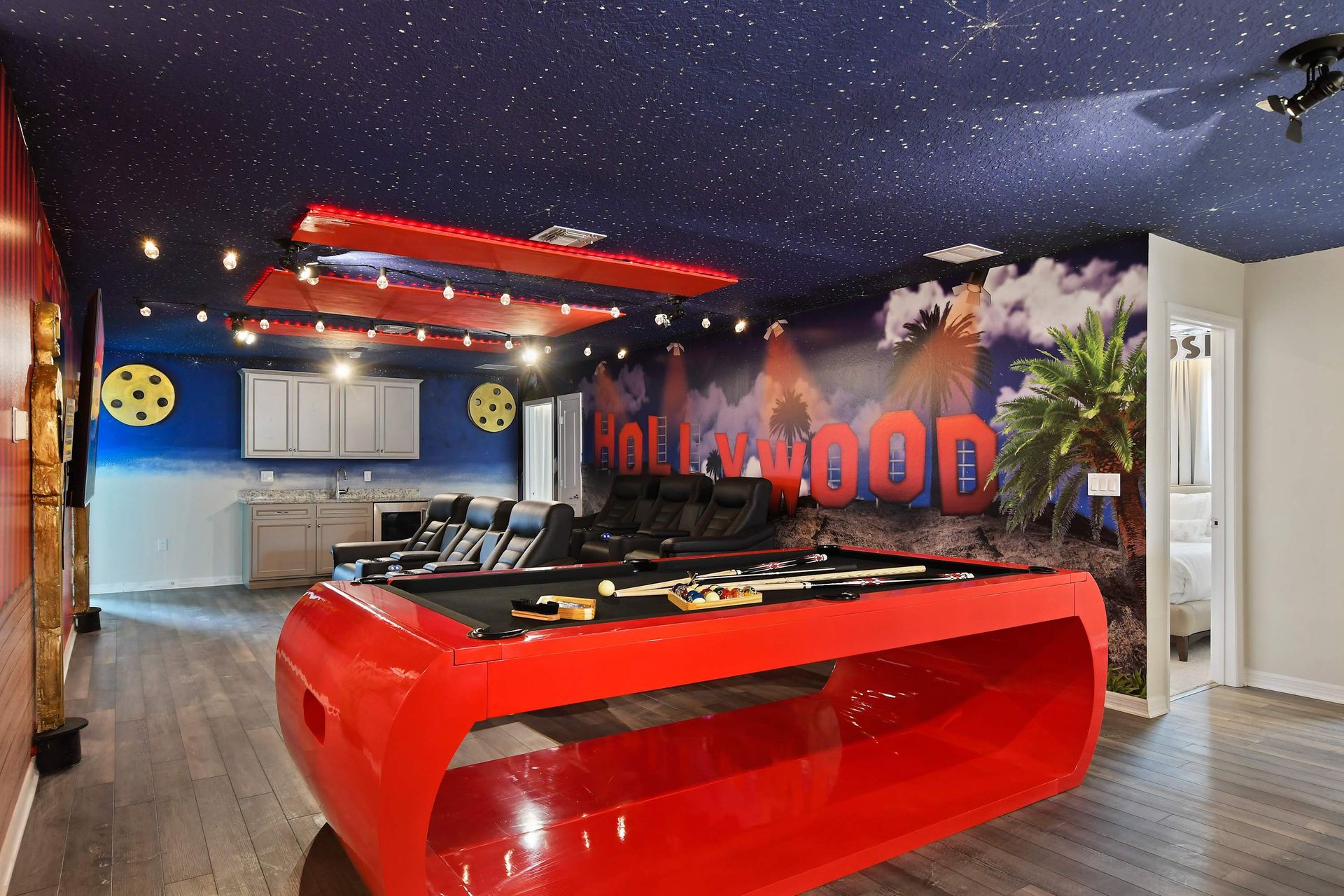 Hollywood-themed game room with red pool table, theater seating, and starry ceiling.