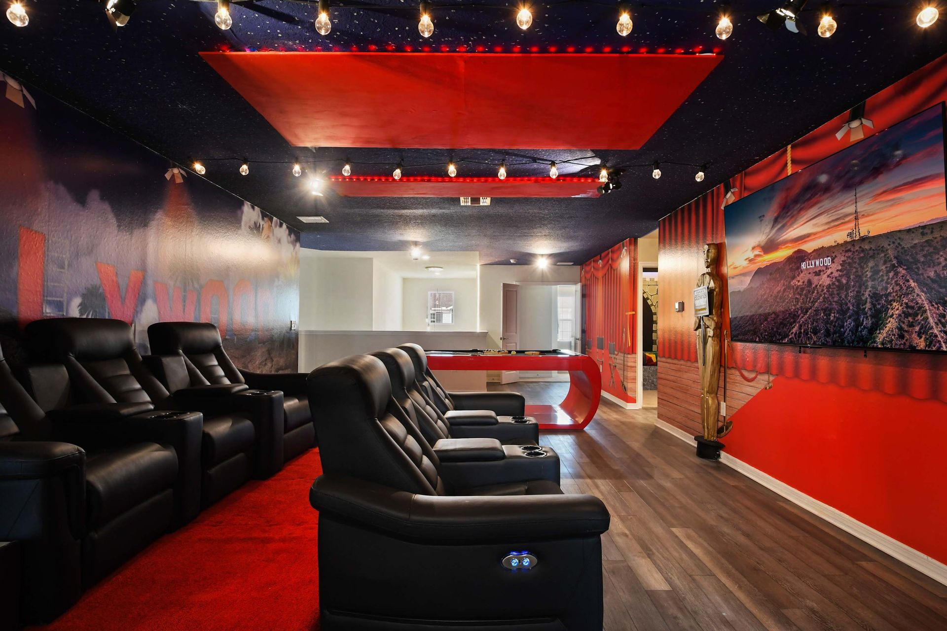 Immersive home theater with recliners, red carpet, Hollywood murals, and pool table.