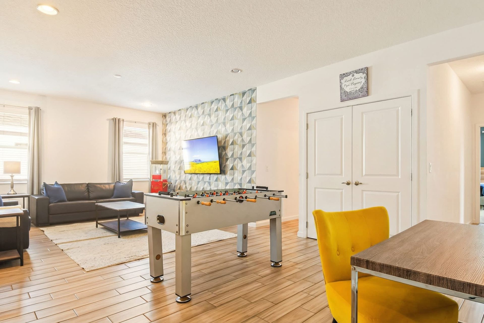 Game room lounge with foosball, TV, workspace, and bold modern accent wall.

