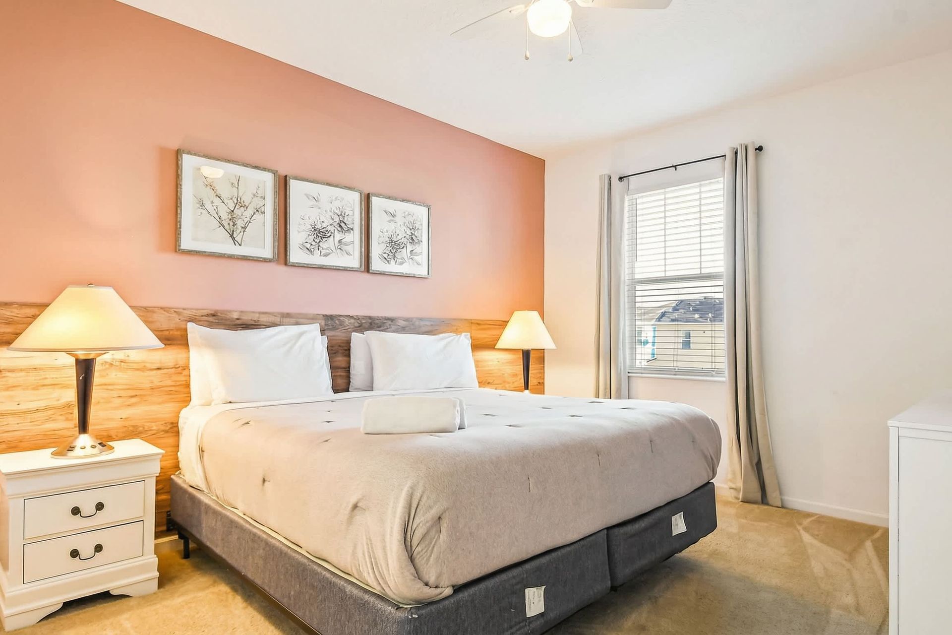 Elegant bedroom with king bed, soft lighting, blush accent wall, and TV.
