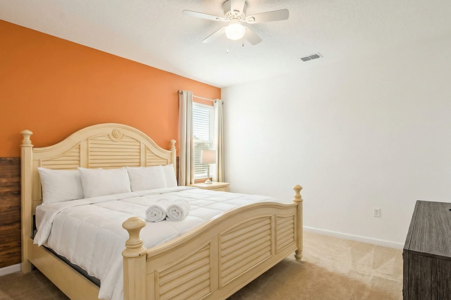 Spacious bedroom with king bed, bold orange accent wall, and cozy natural light.
