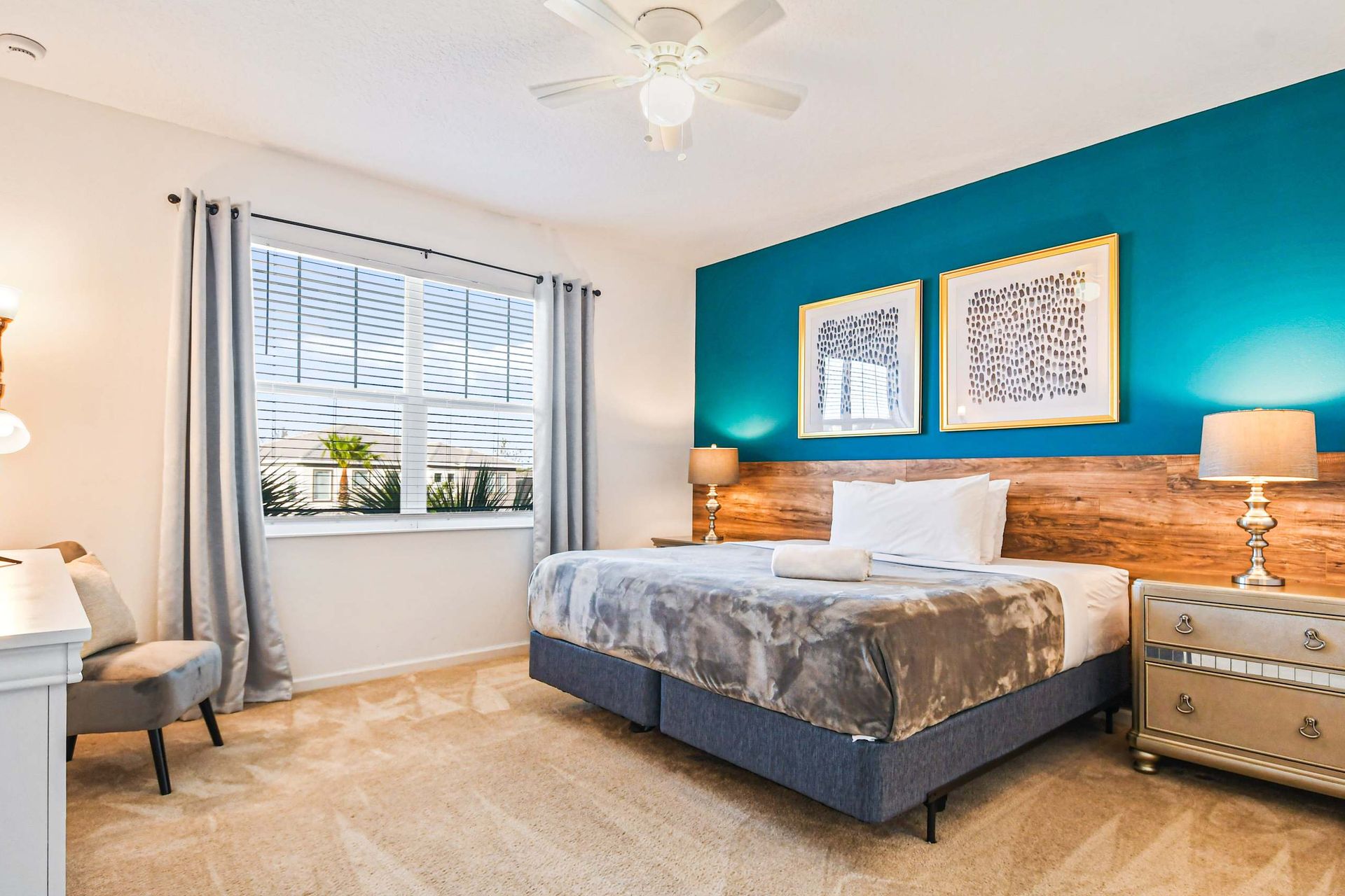 Stylish king bedroom with bold teal accent wall, natural light, and cozy decor.
