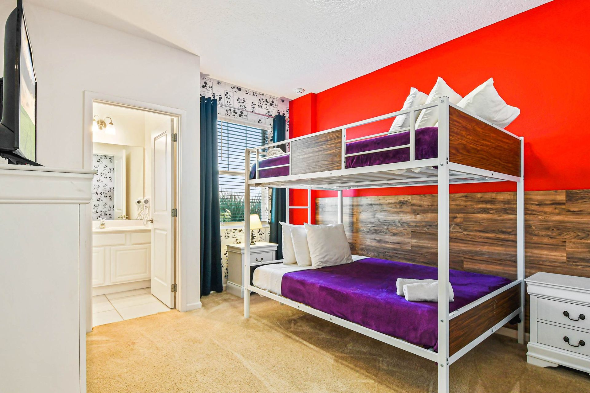 Colorful bunk room with bold red accent wall, purple bedding, and private bath.
