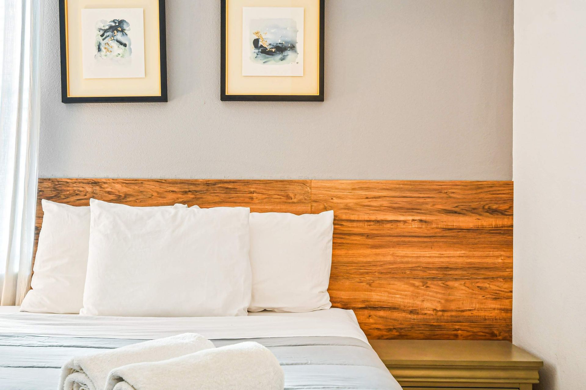 Cozy bed setup with wood headboard, soft linens, and calming wall art.
