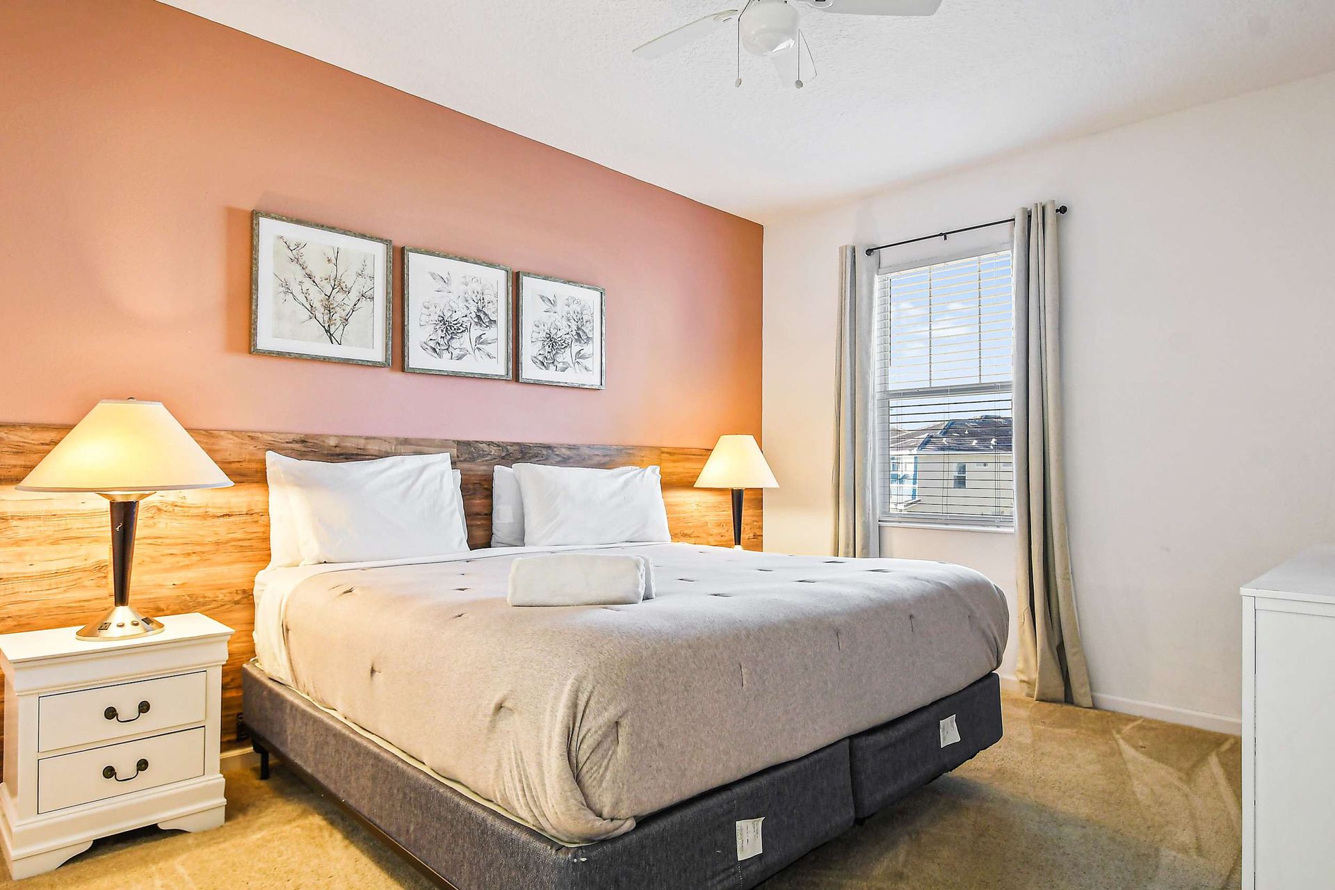 Elegant bedroom with king bed, soft lighting, blush accent wall, and TV.
