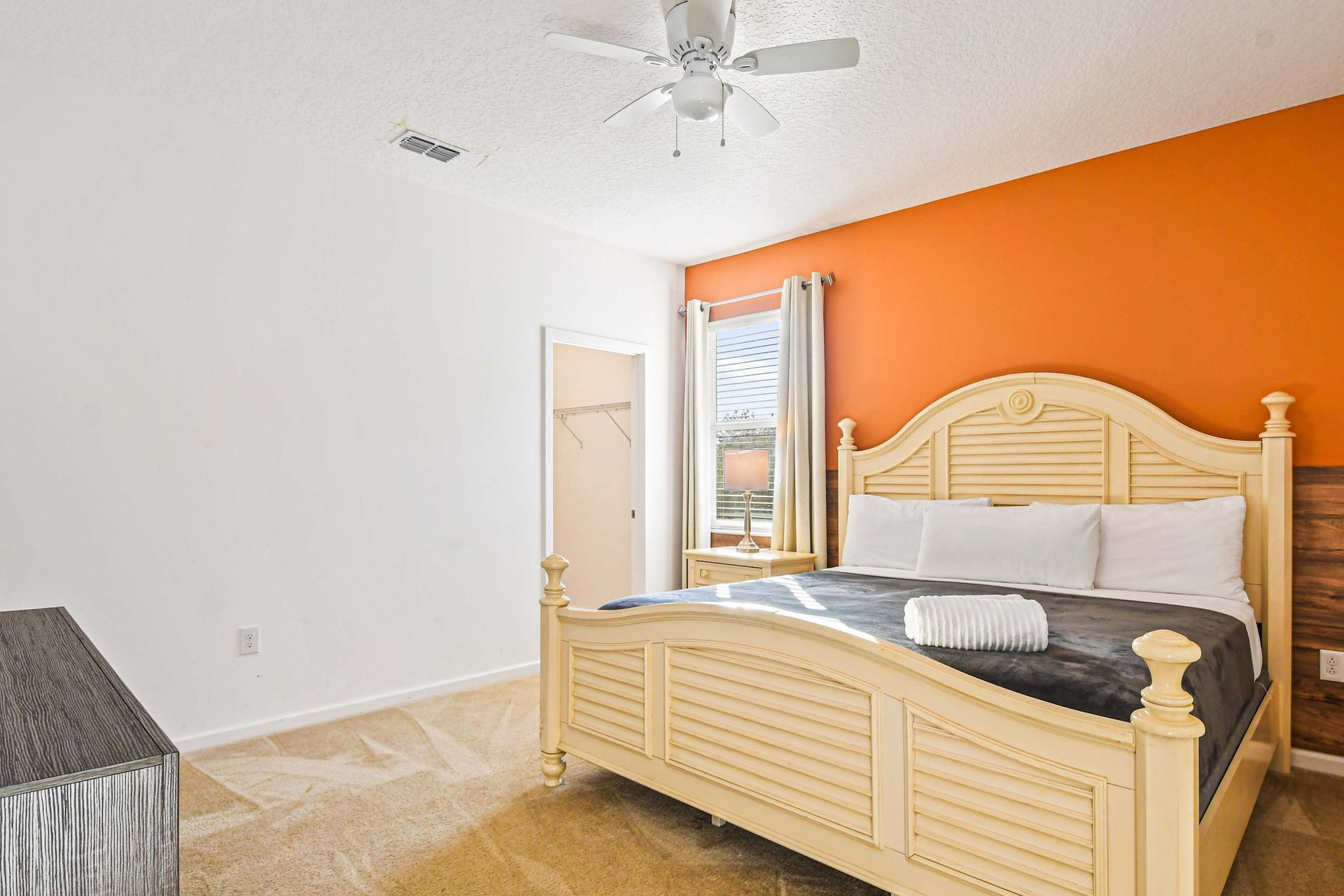 Spacious bedroom with king bed, bold orange accent wall, and cozy natural light.
