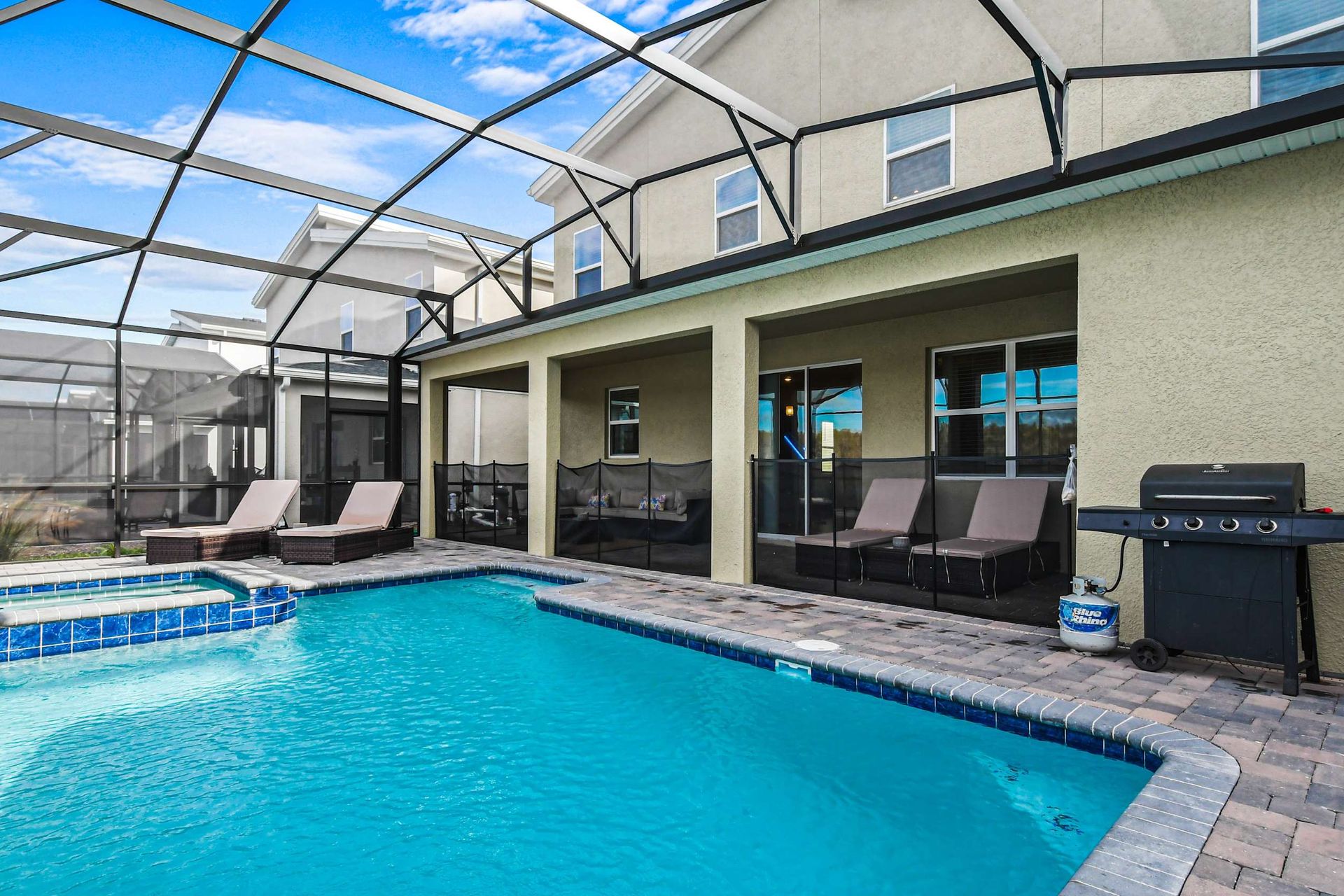 Spacious screened pool area with spa, BBQ grill, loungers, and outdoor seating.