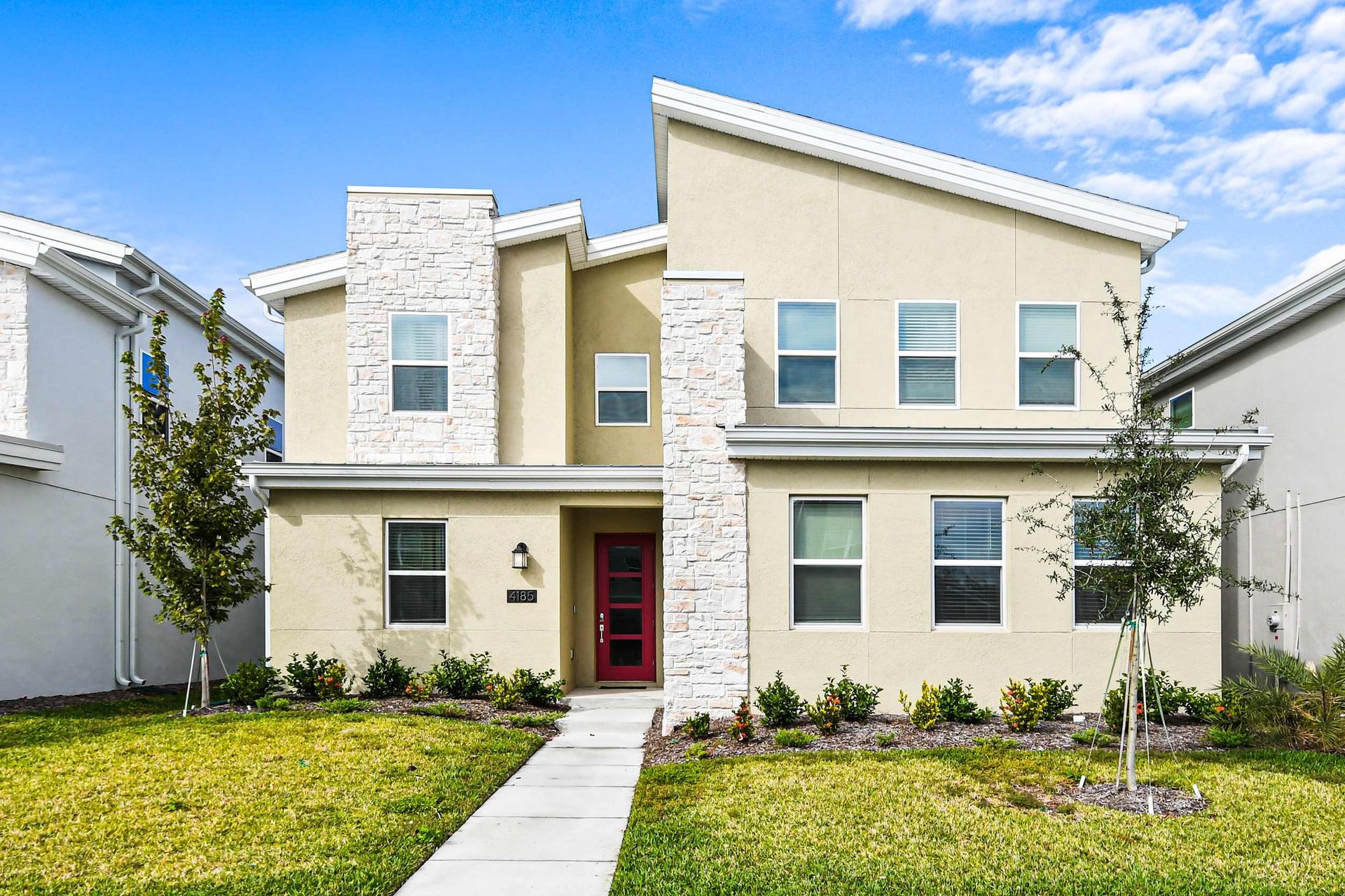 Modern 2-story retreat with bold red door, sleek stone accents, and lush yard charm.