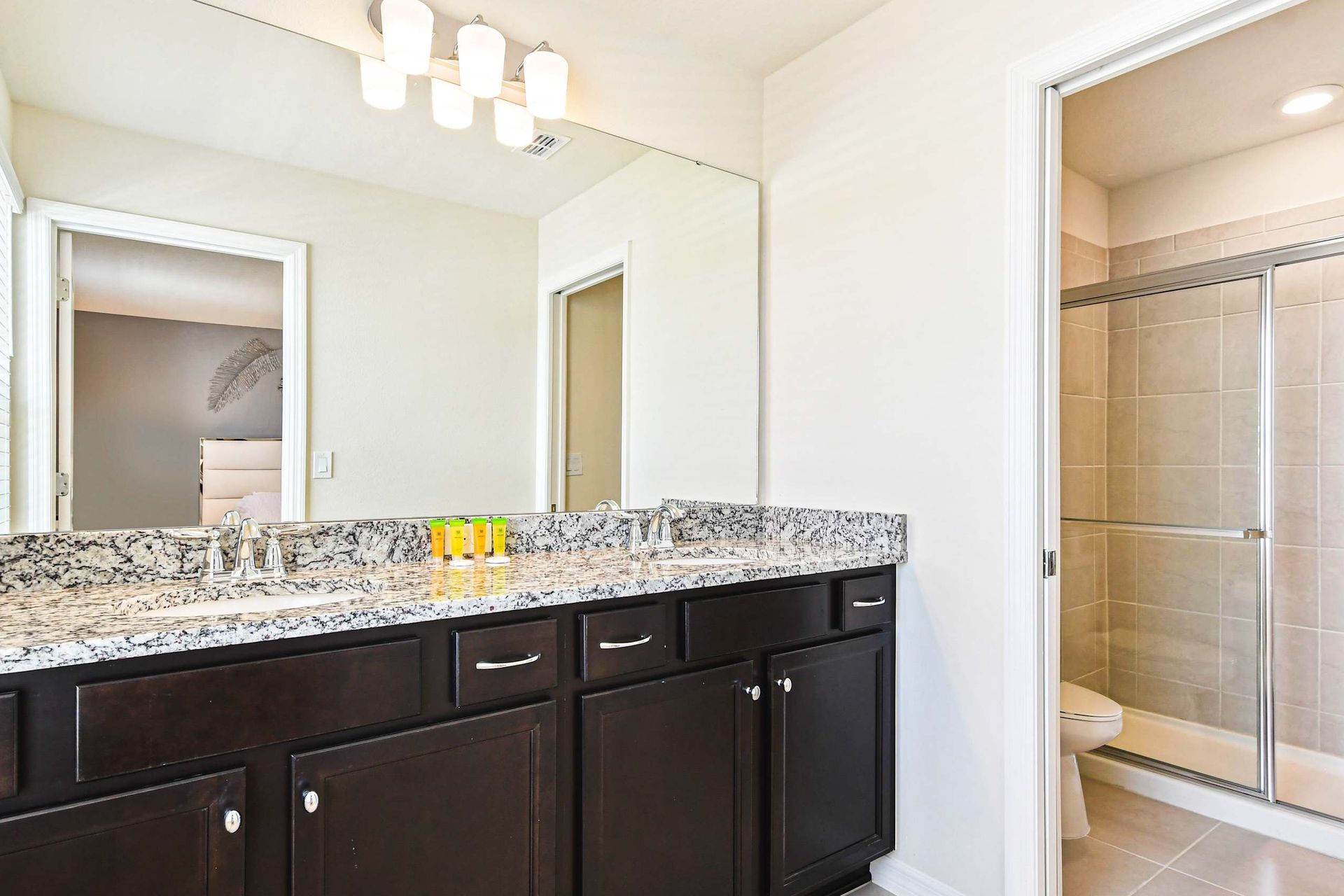 Modern bathroom with granite double vanity, large mirror, and glass walk-in shower