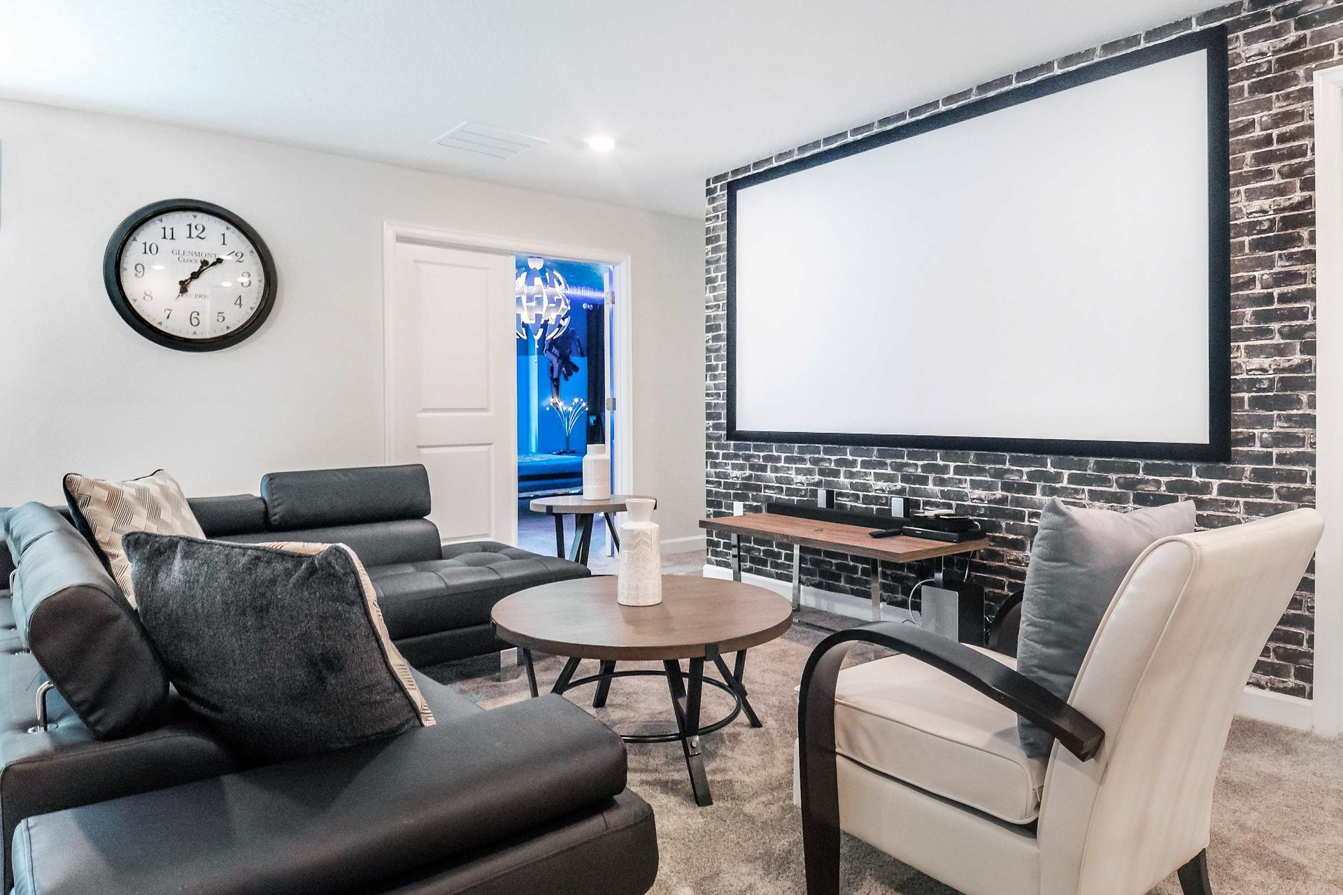 Cozy home theater with a brick accent wall, plush seating, and a large screen.
