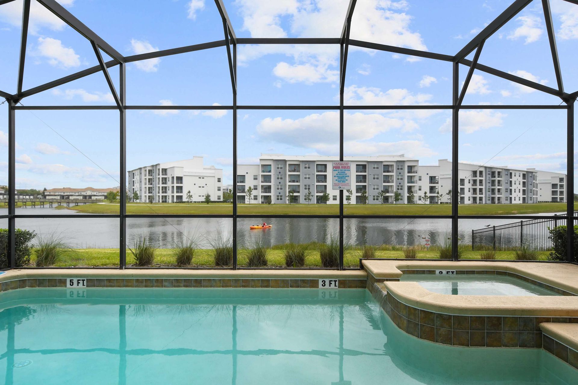 Serene lakefront screened pool and spa with peaceful views of modern apartments across the water.