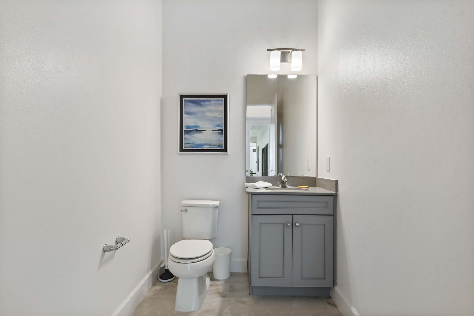 Cozy half bath with sleek vanity, modern lighting, and calming coastal artwork.
