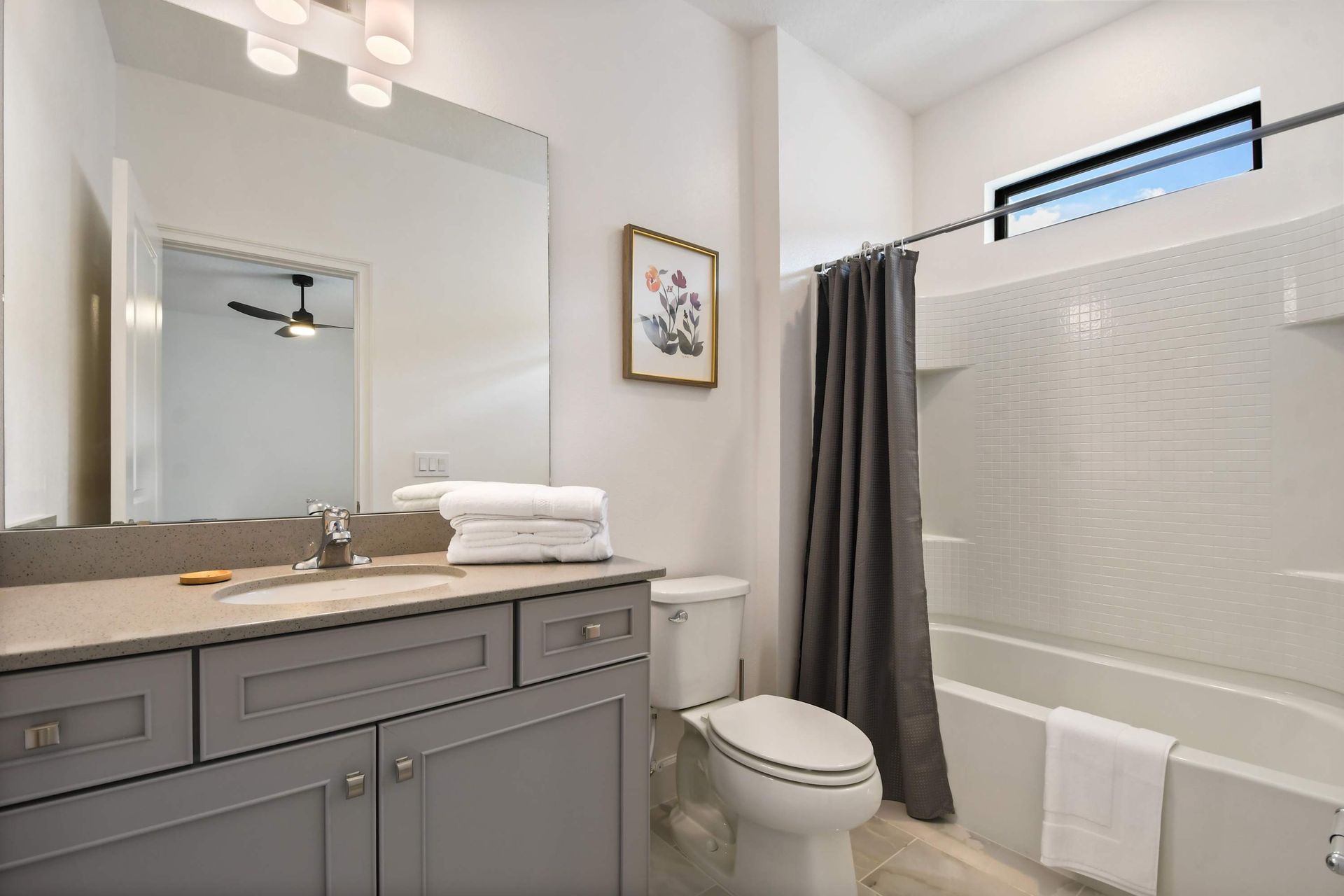 Elegant full bathroom with modern vanity, floral artwork, and bright natural light.