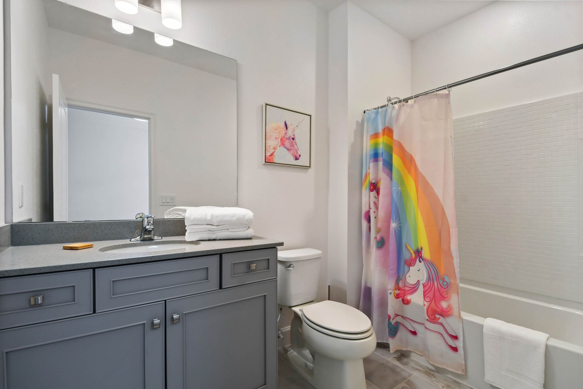 Magical unicorn-themed bathroom with rainbow shower curtain and modern vanity style.